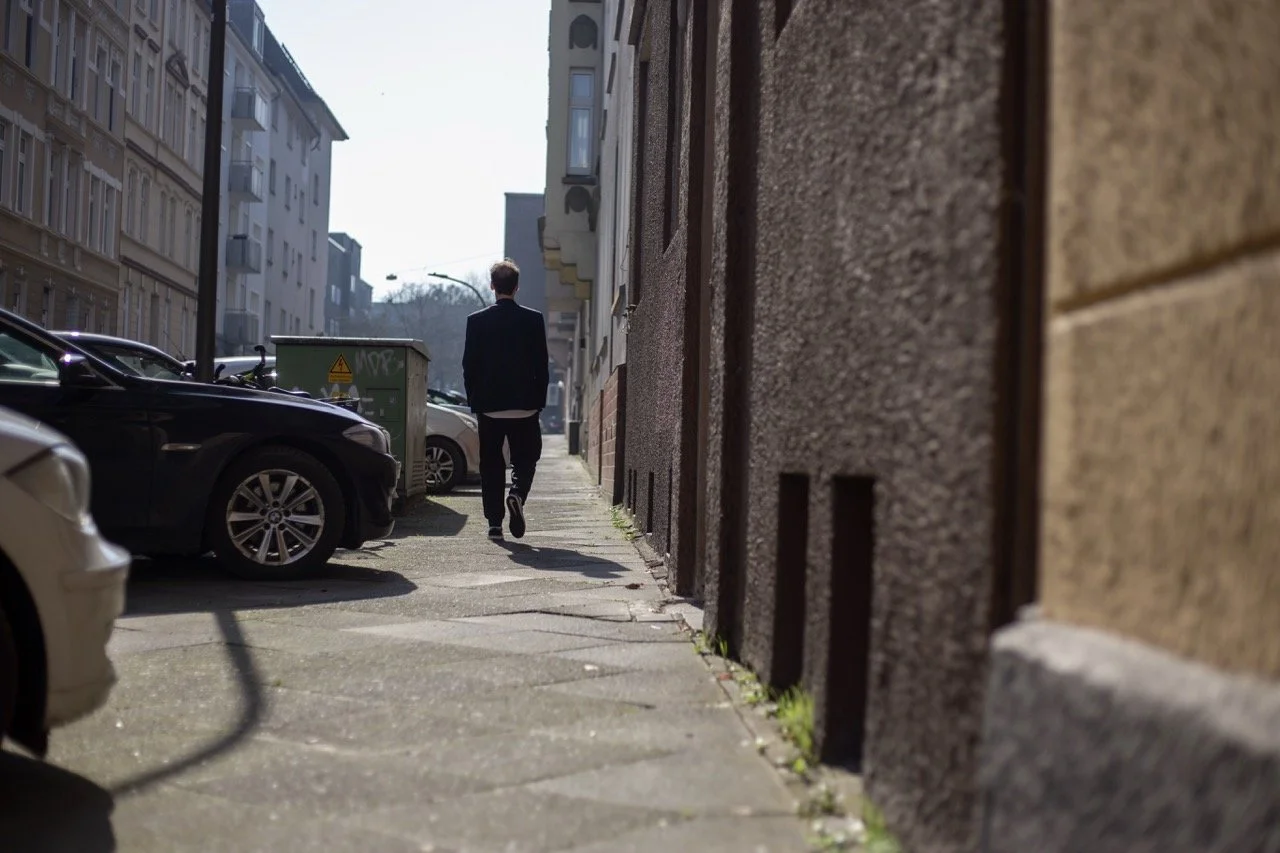 Thomas Ploch, spazierend mit Händen in den Taschen und von hinten fotografiert
