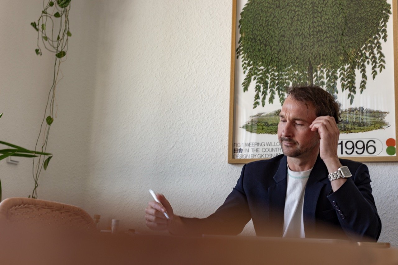 Thomas Ploch nachdenklich mit einem Stift in der Hand an einem Tisch sitzend