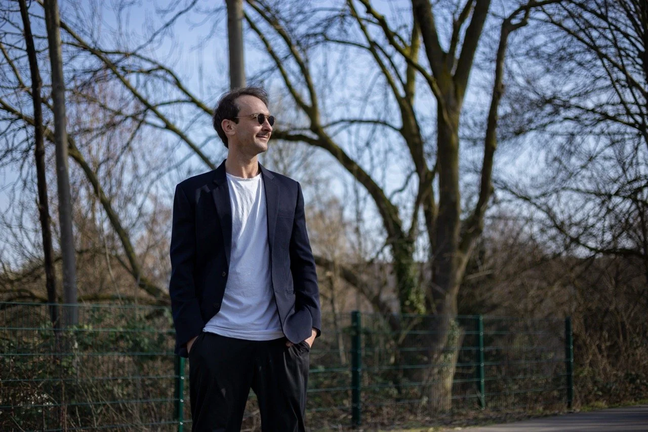 Thomas Ploch mit Sonnenbrille und Anzug, in die Ferne schauend