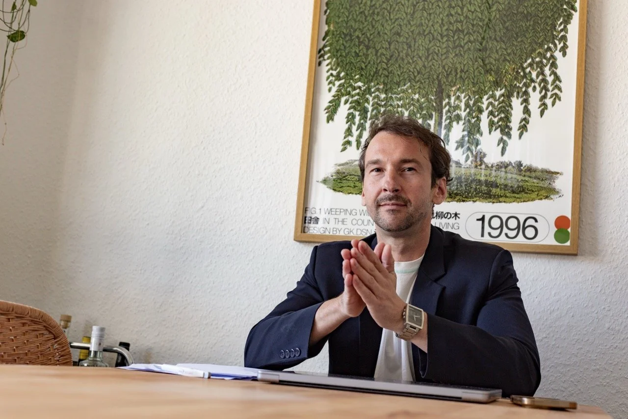 Thomas Ploch zuversichtlich sitzend am Tisch und in die Kamera schauend