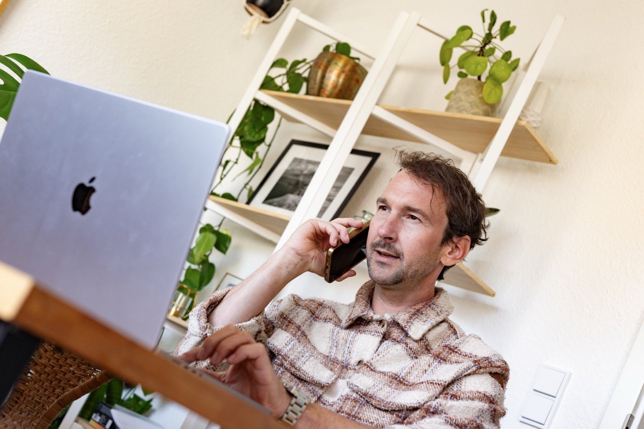 Thomas Ploch wie er vor einem MAcbook sitzt und dabei telefoniert