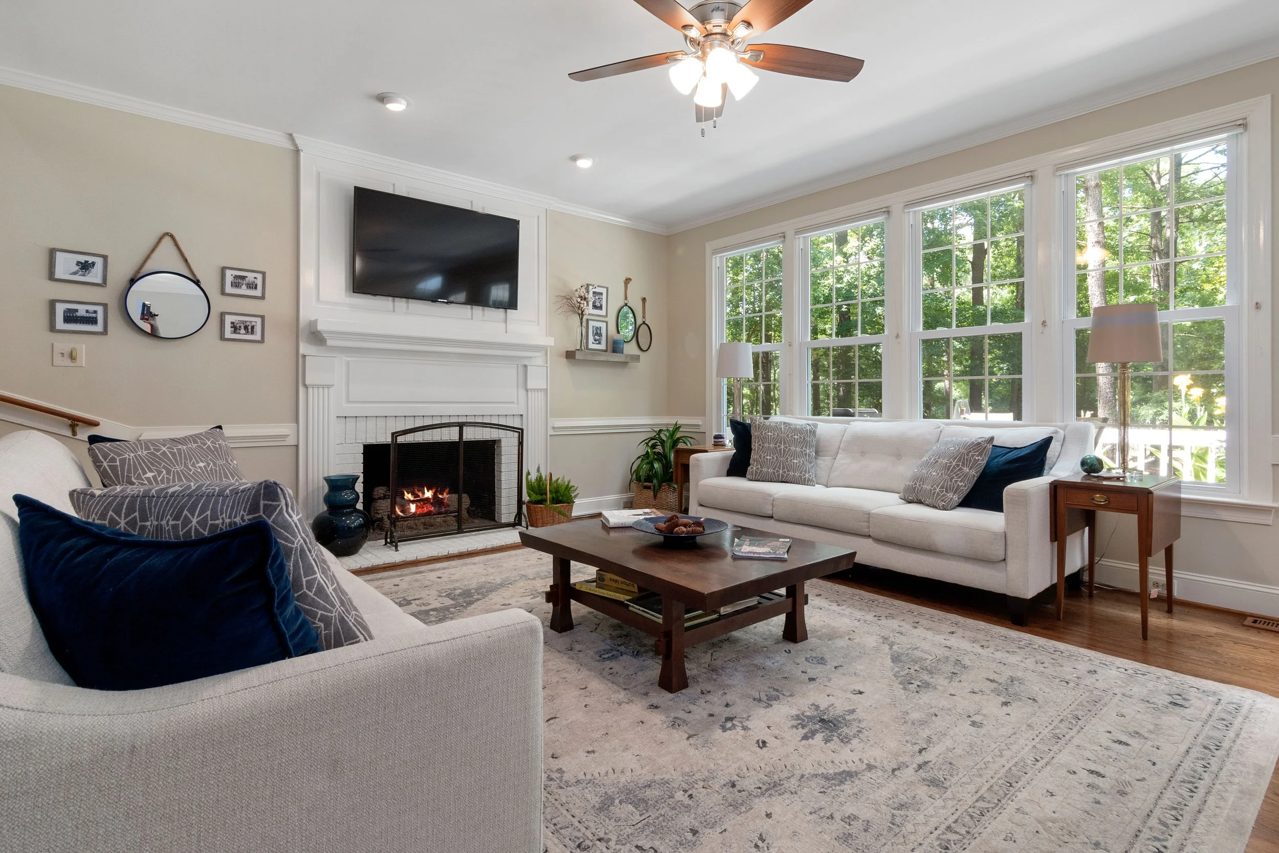 Spacious family living space with grey couches, a large white fireplace, wall mounted tv and dark wooden furniture.