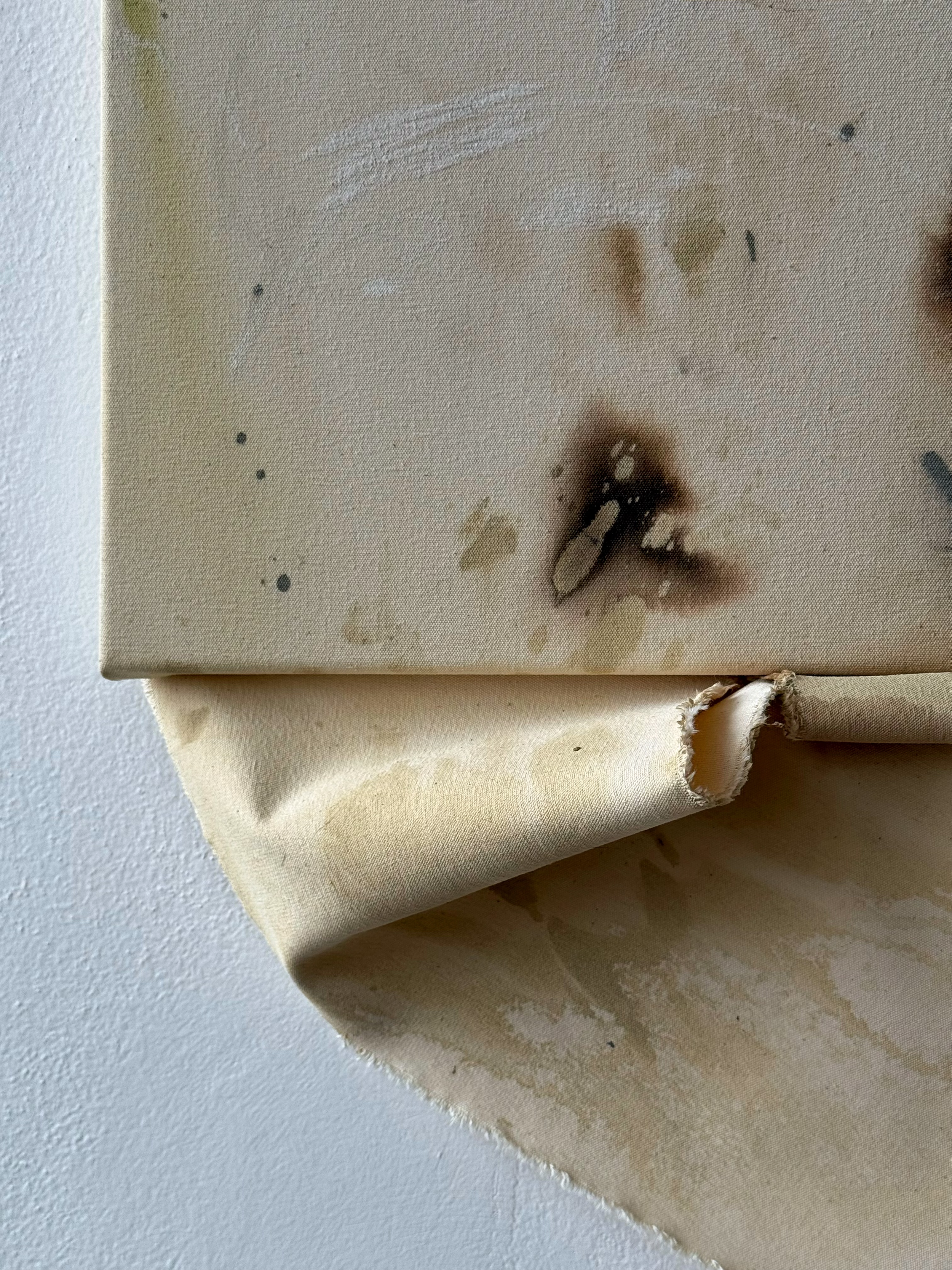 Close-up of a textured canvas with visible paint splatters in beige, brown, and black on a draped beige cloth surface.