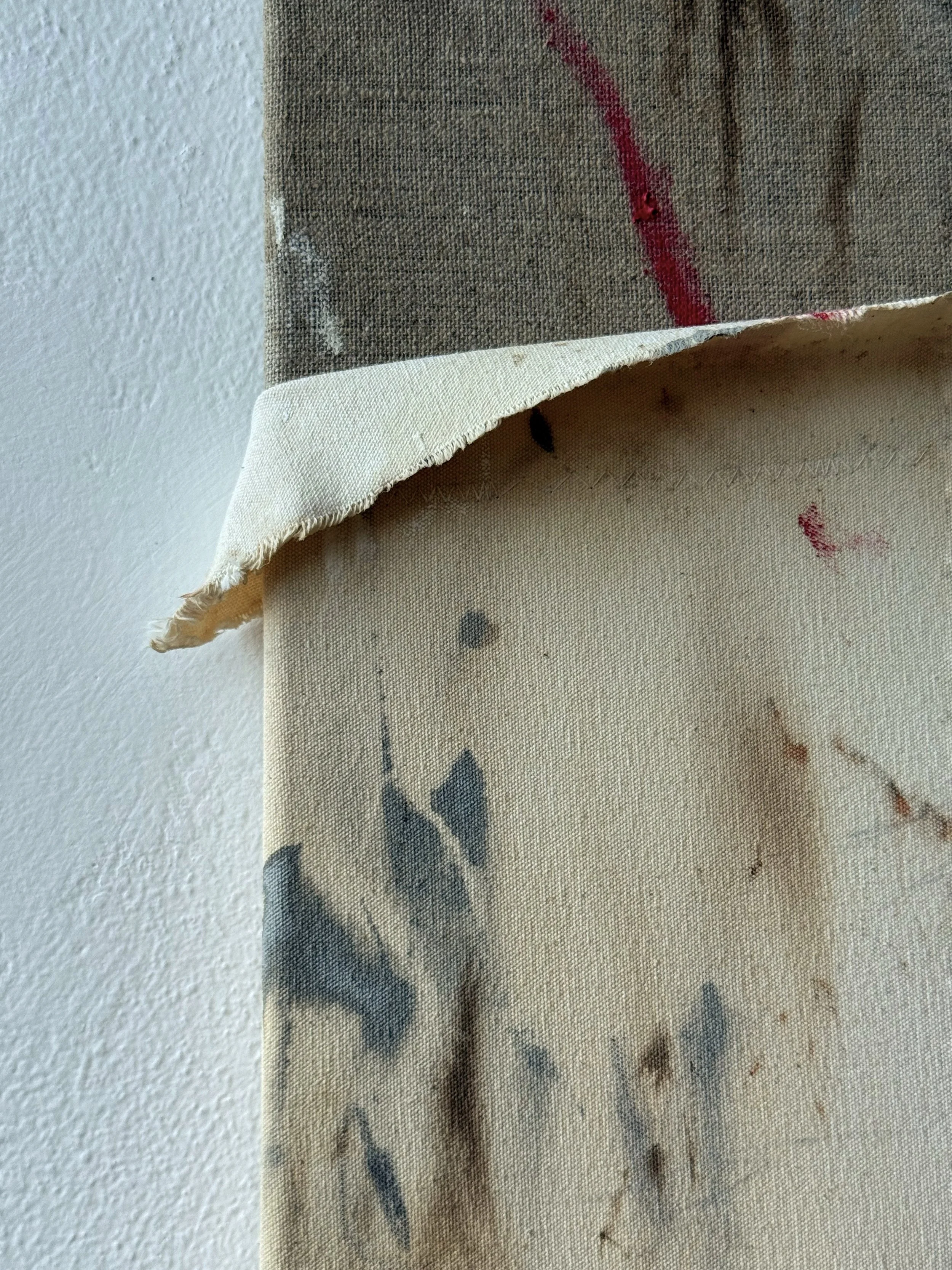 Close-up of a fabric with a floral pattern, showing a corner folded back, revealing a plain beige underside with some stains and discoloration.
