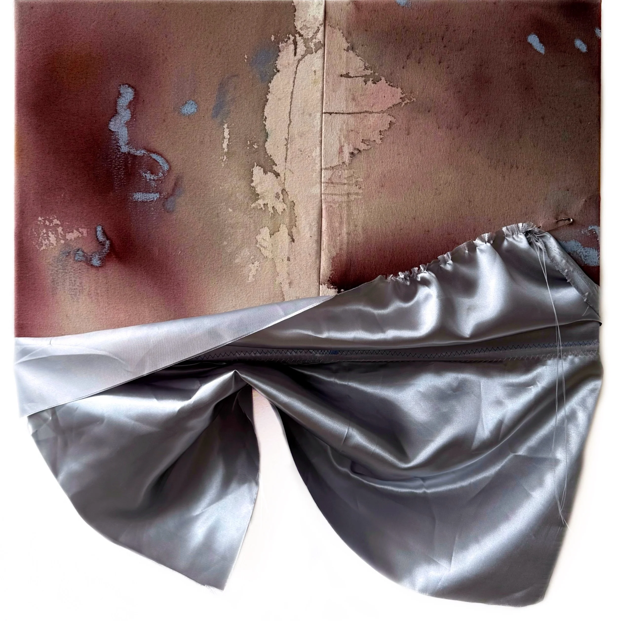 Close-up of a textured, irregularly torn paper with layers of brown, beige, and gray, and a small section of crumpled silver metallic paper at the corner.