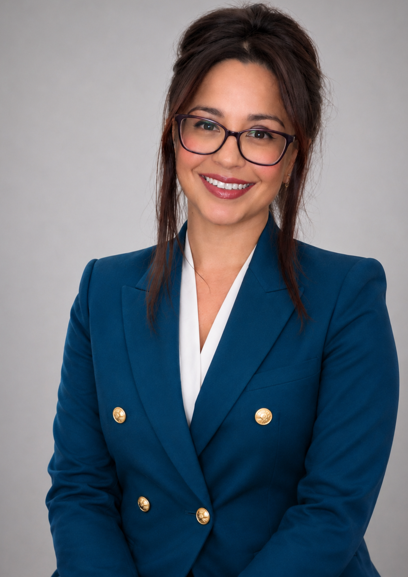Natasha - With shoulder-length brown hair, glasses, and a smile, wearing a dark blue blazer with gold buttons and a white shirt, standing against a plain gray background - Ascension Real Estate property management Melbourne West