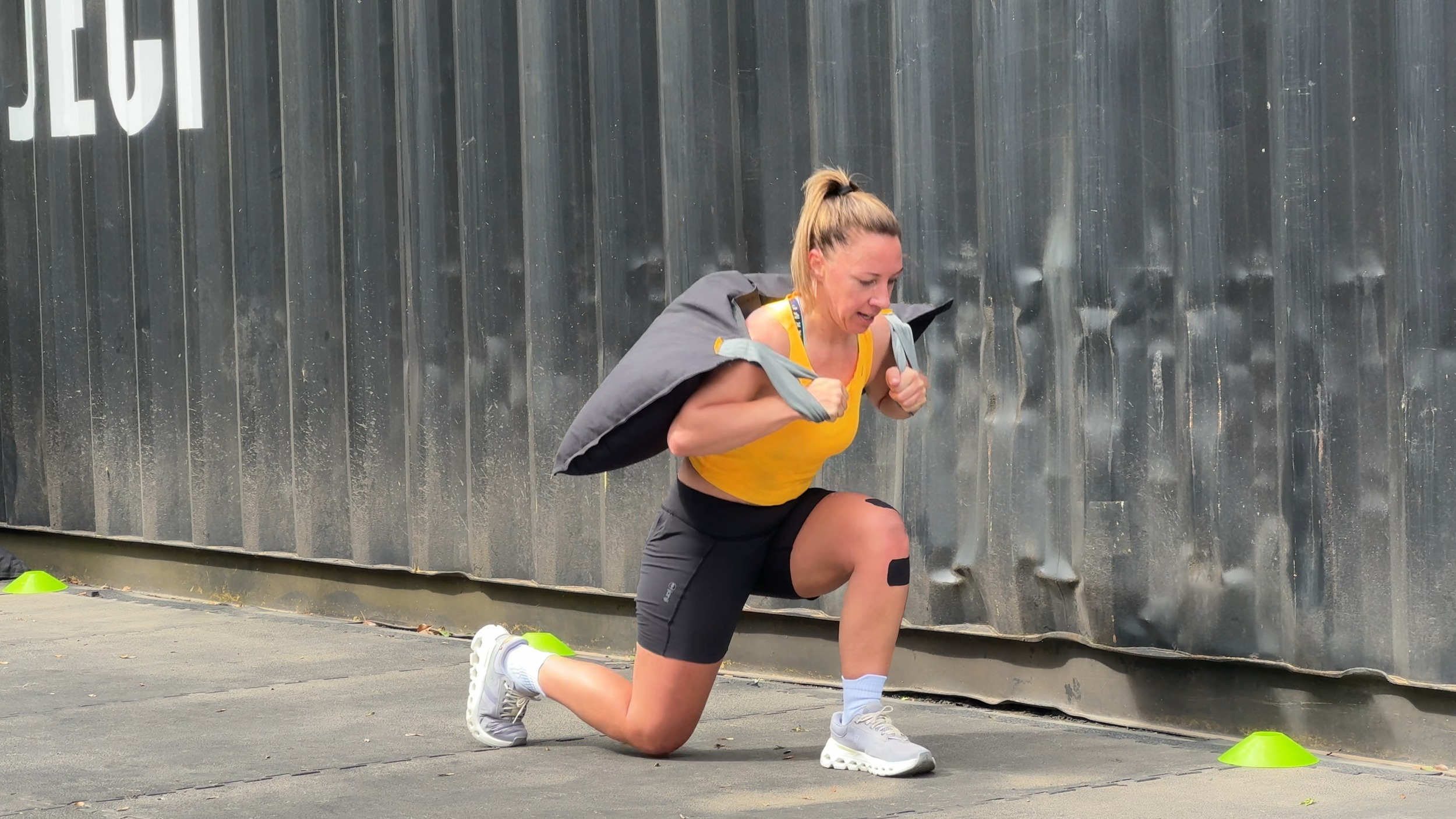female doing a lunge exercise with heavy sandbag bag over shoulders