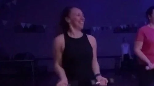 a woman in black fitness clothing with weights in hand, smiling and dancing
