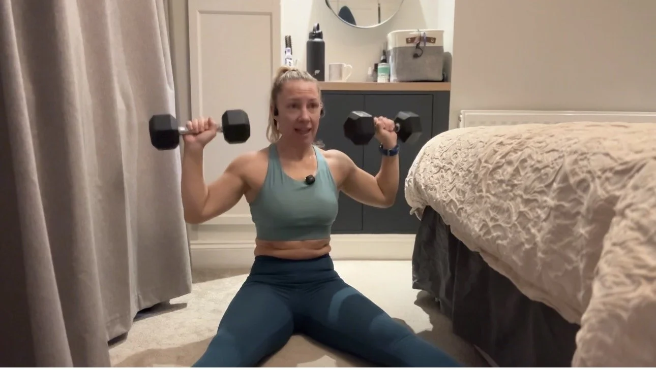 female in teal workout outfit performing a shoulder press with 2 hex dumbbells