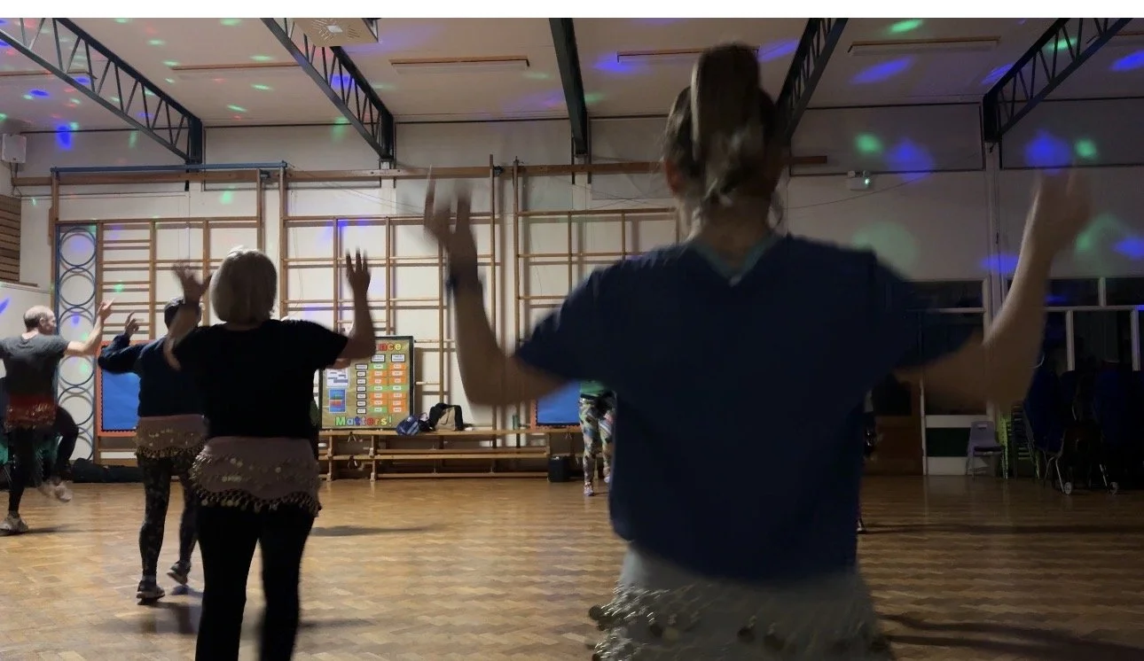 a dance fitness class, viewing women from behind with arms in the air dancing