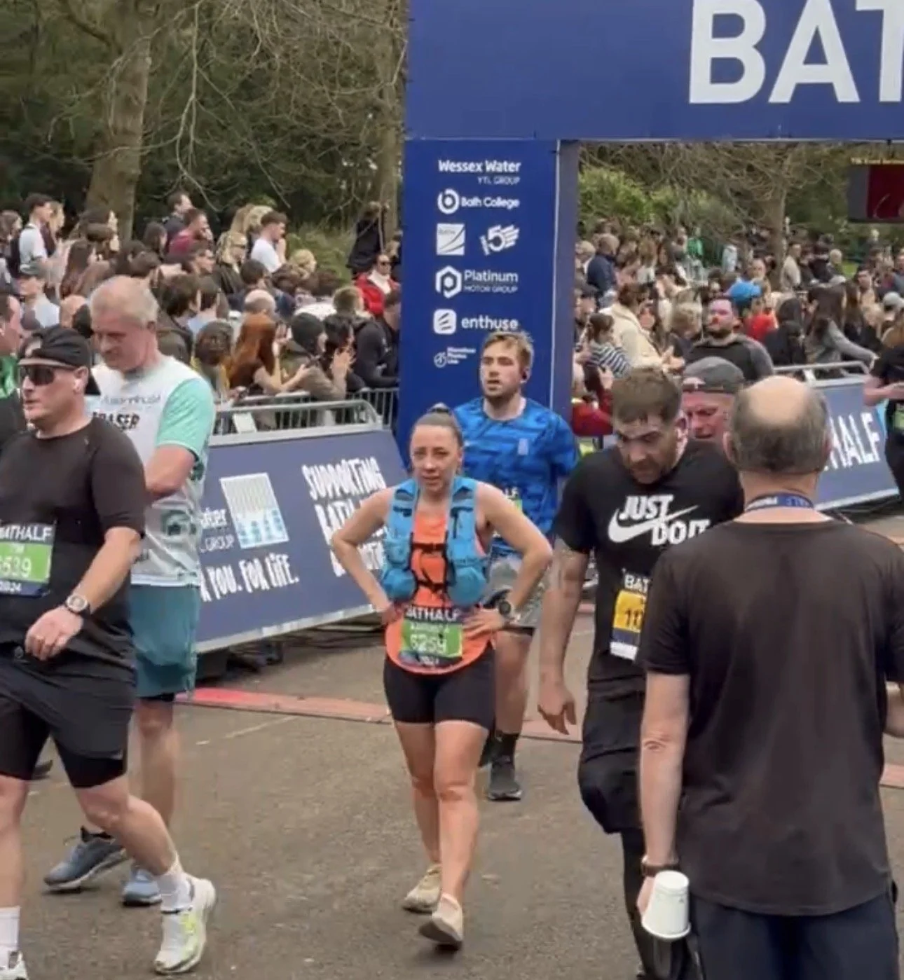 Bath Half Finish Line and woman looking tired after finishing, other runners and crowd