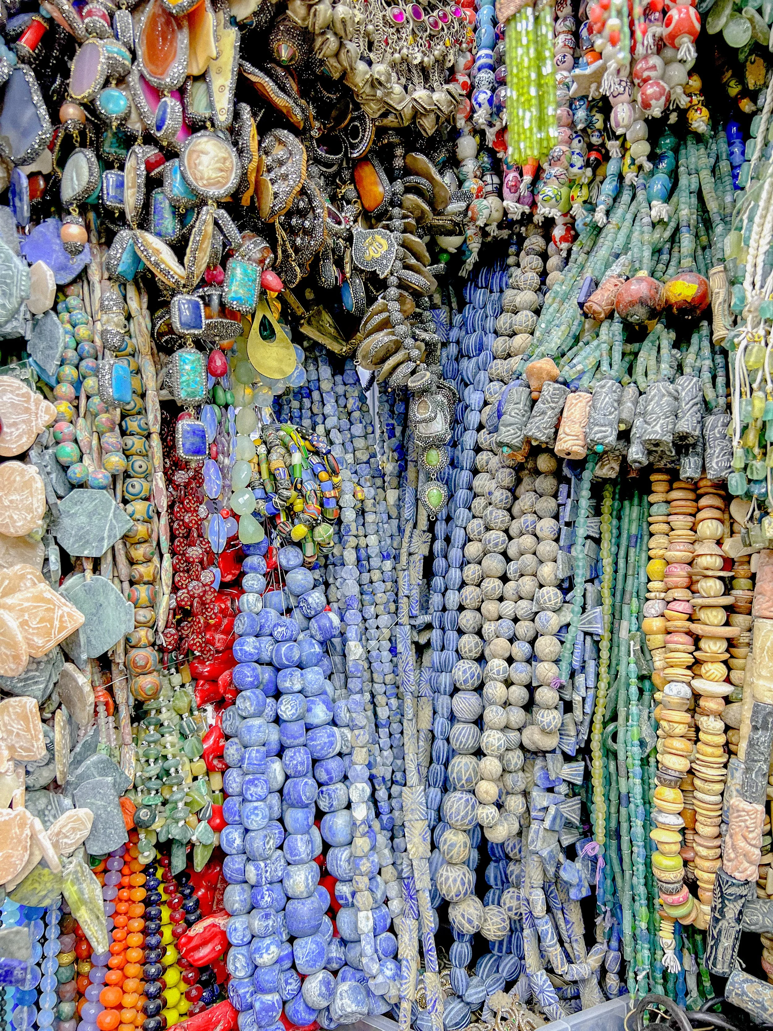 Colorful display of various beaded necklaces and jewelry made from different types of stones, shells, and materials, hanging closely together.