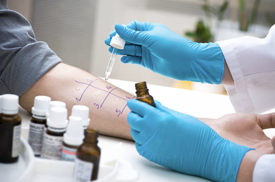 Person receiving a blood draw from healthcare professional wearing blue gloves, with blood collection bottles on the table.