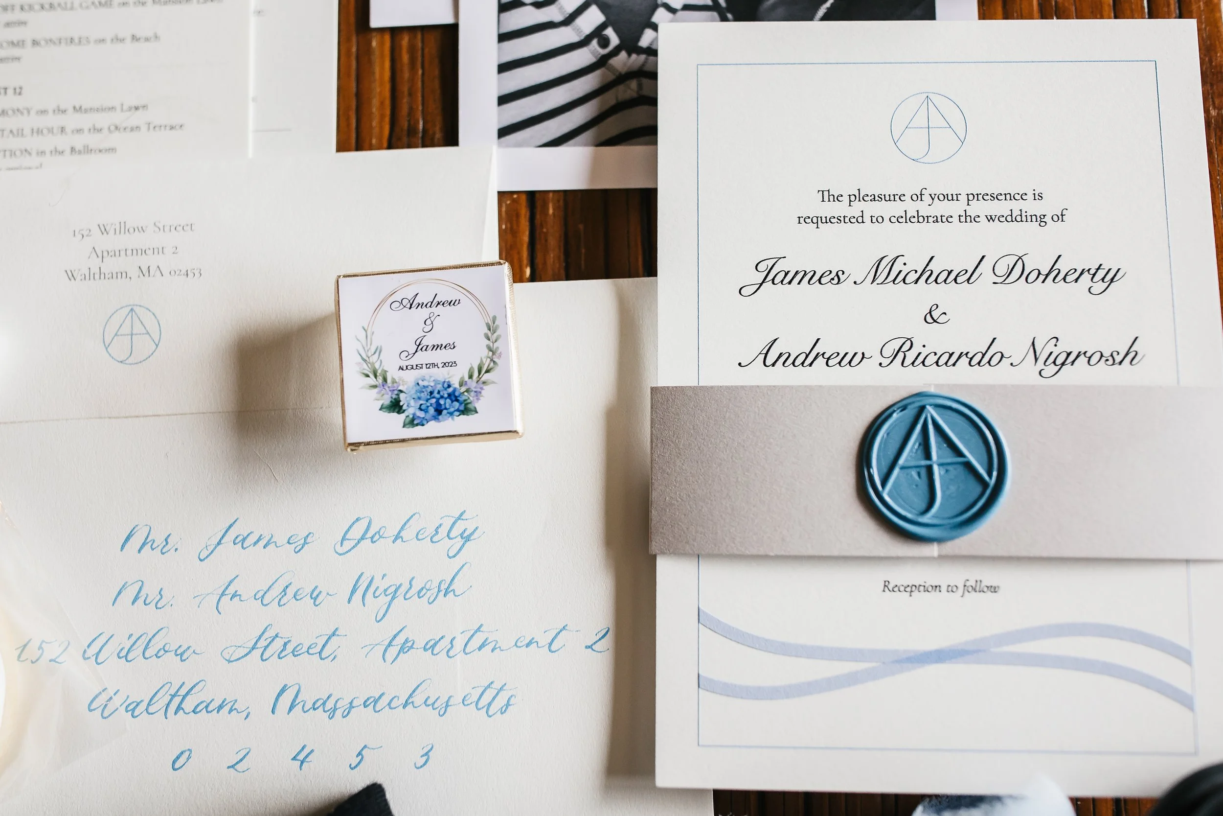 Wedding invitation suite and small box with floral design, featuring wedding details for James Michael Doherty and Andrew Ricardo Nigrosh, including envelopes with handwritten addresses and a blue wax seal.