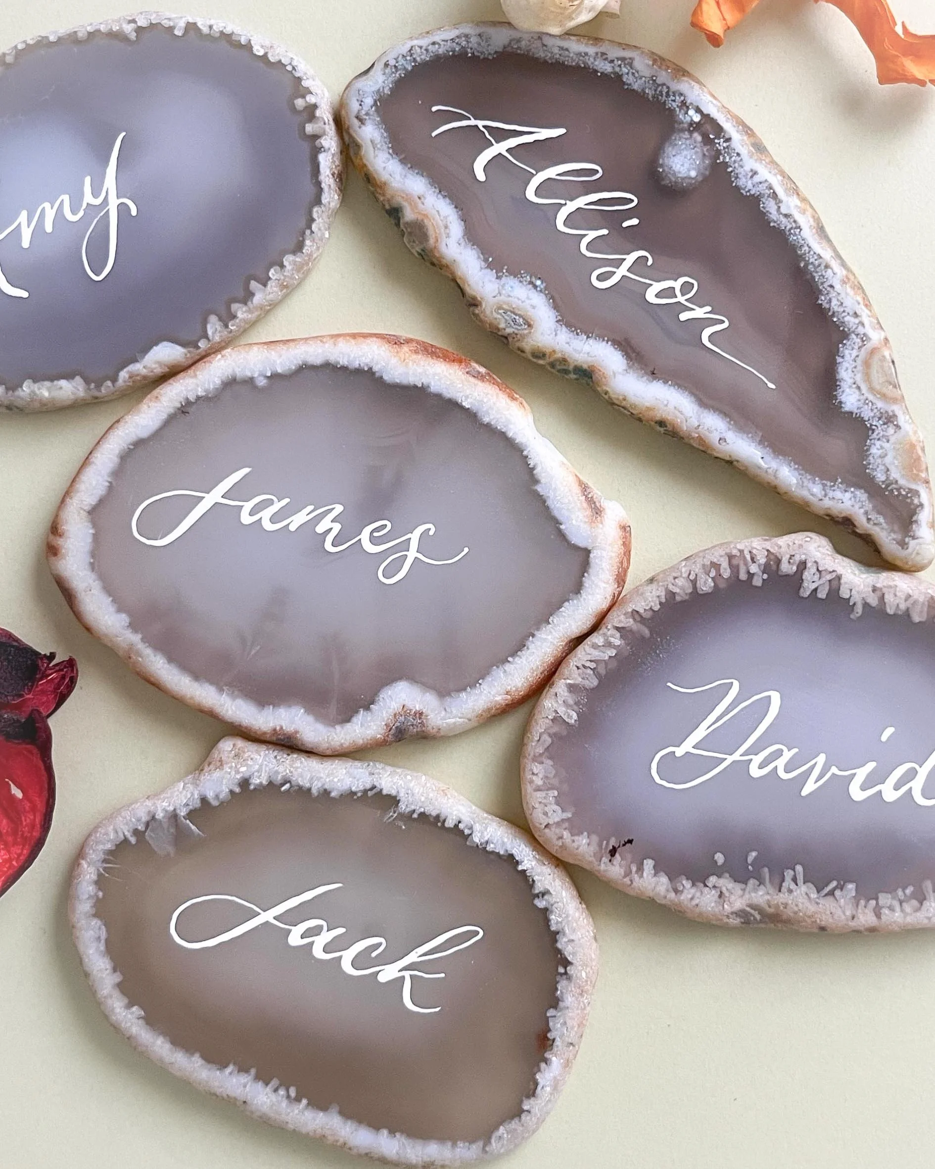 Painted agate coasters with names written in cursive: Amy, Alison, James, David, Jack, on a light-colored surface.