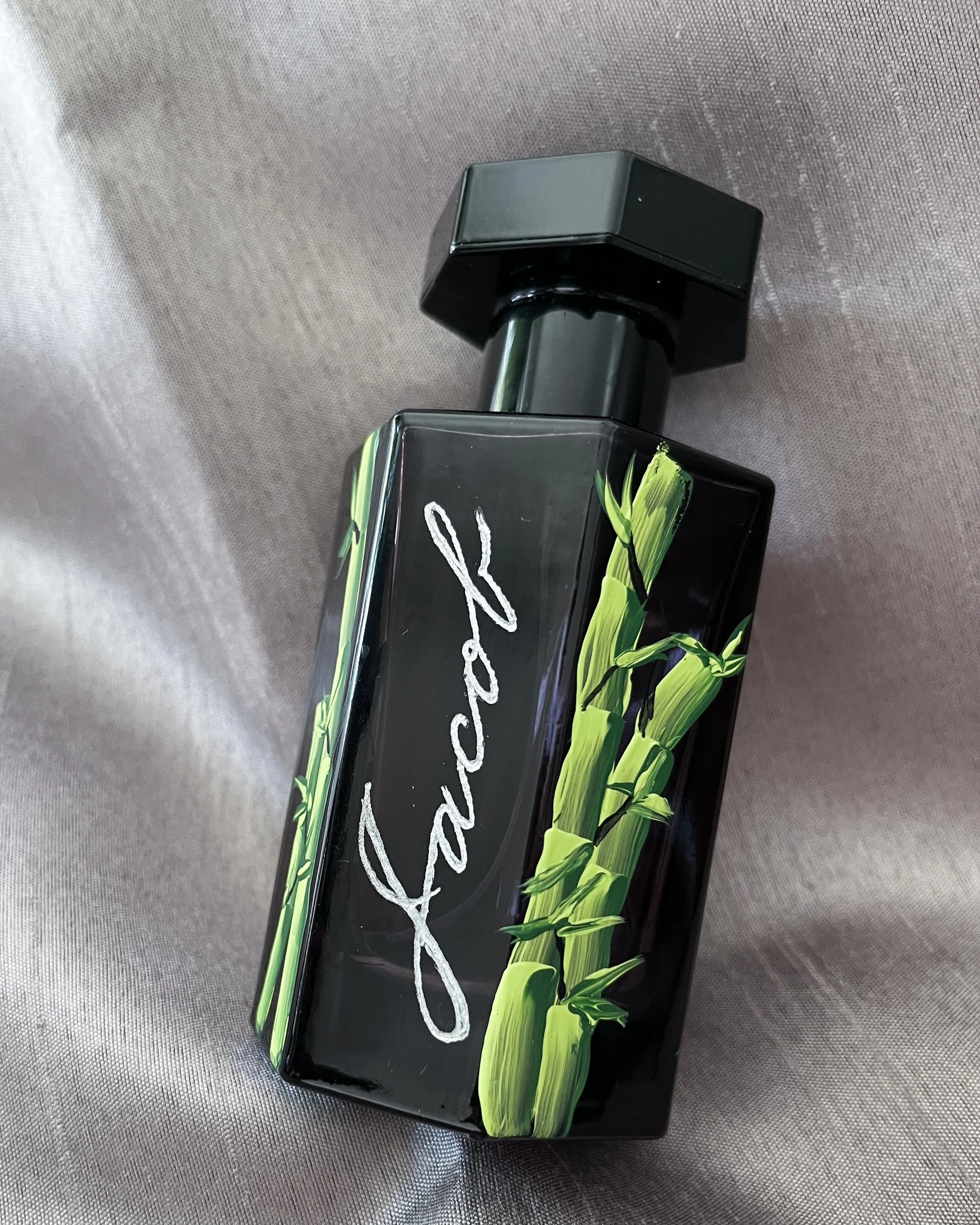 Black perfume bottle with green bamboo design and the name Schwab on it, lying on silk fabric.