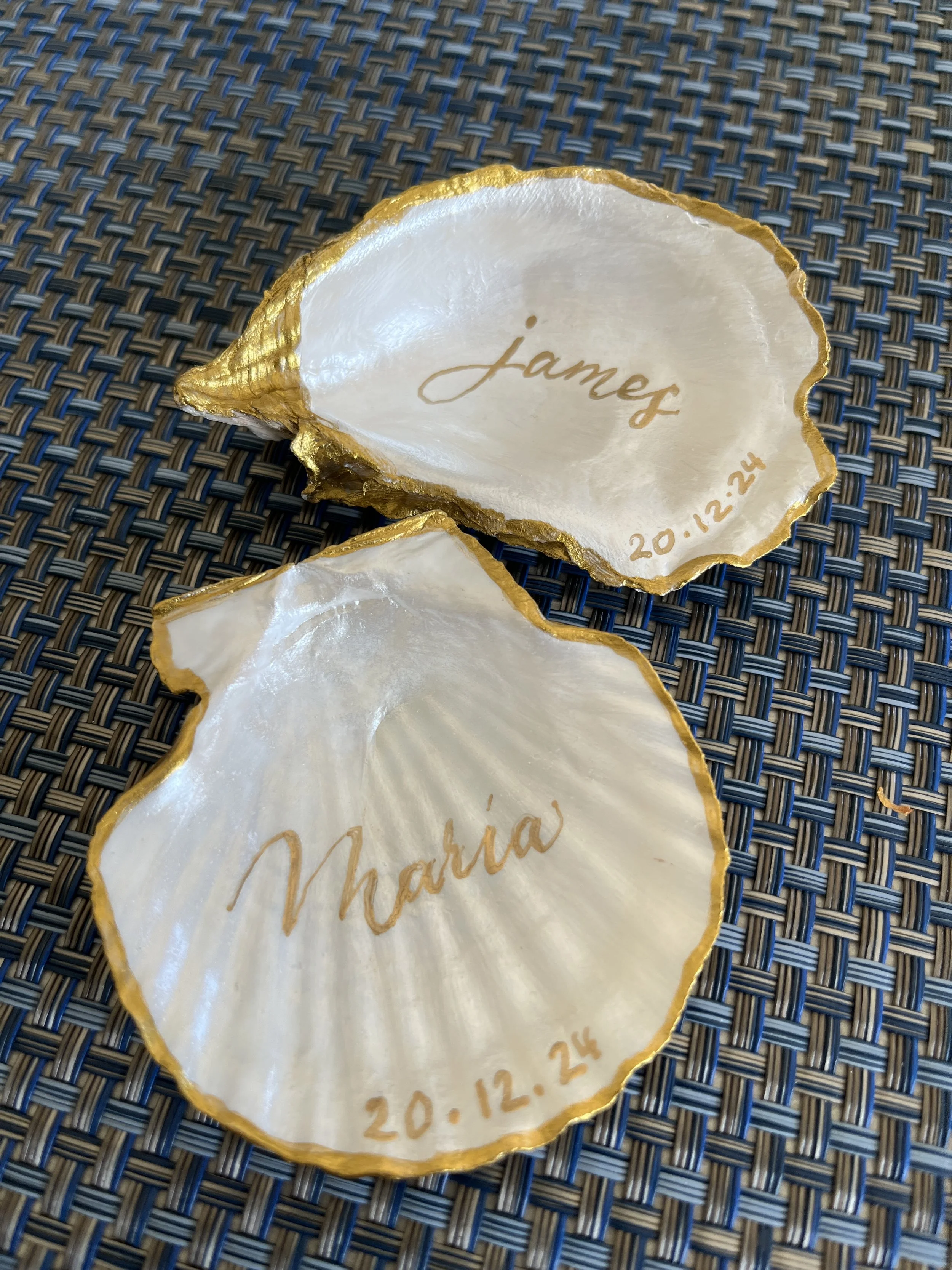 Decorative seashells with gold edges, engraved with the names 'James' and 'Marnia', and wedding dates '20.12.24' engraved inside.