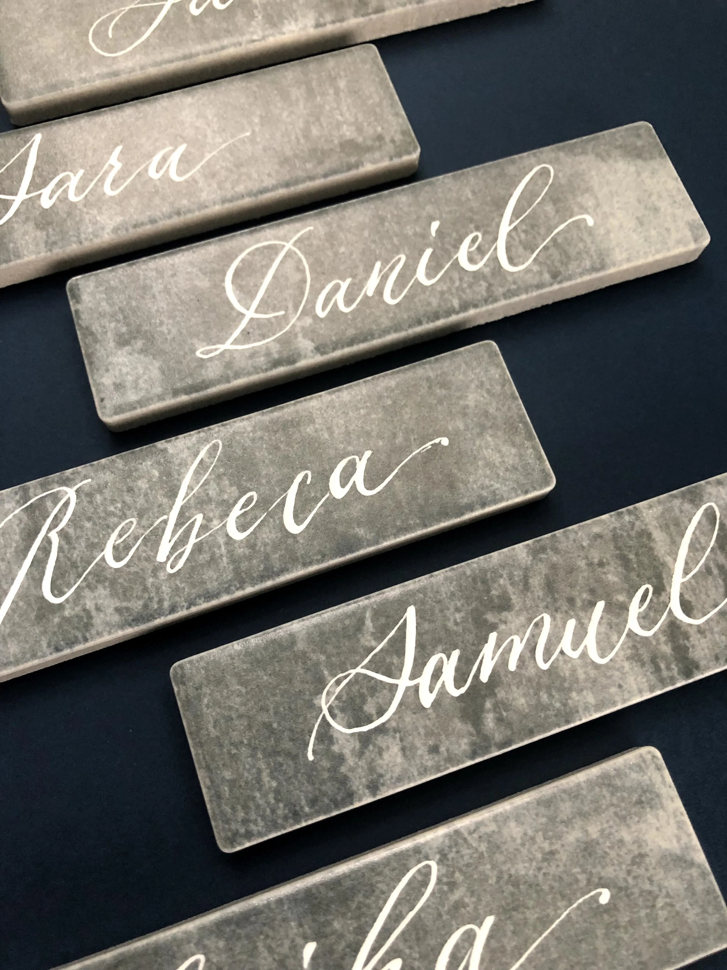 Gray marble nameplates with white cursive writing of different names, arranged on a dark surface.