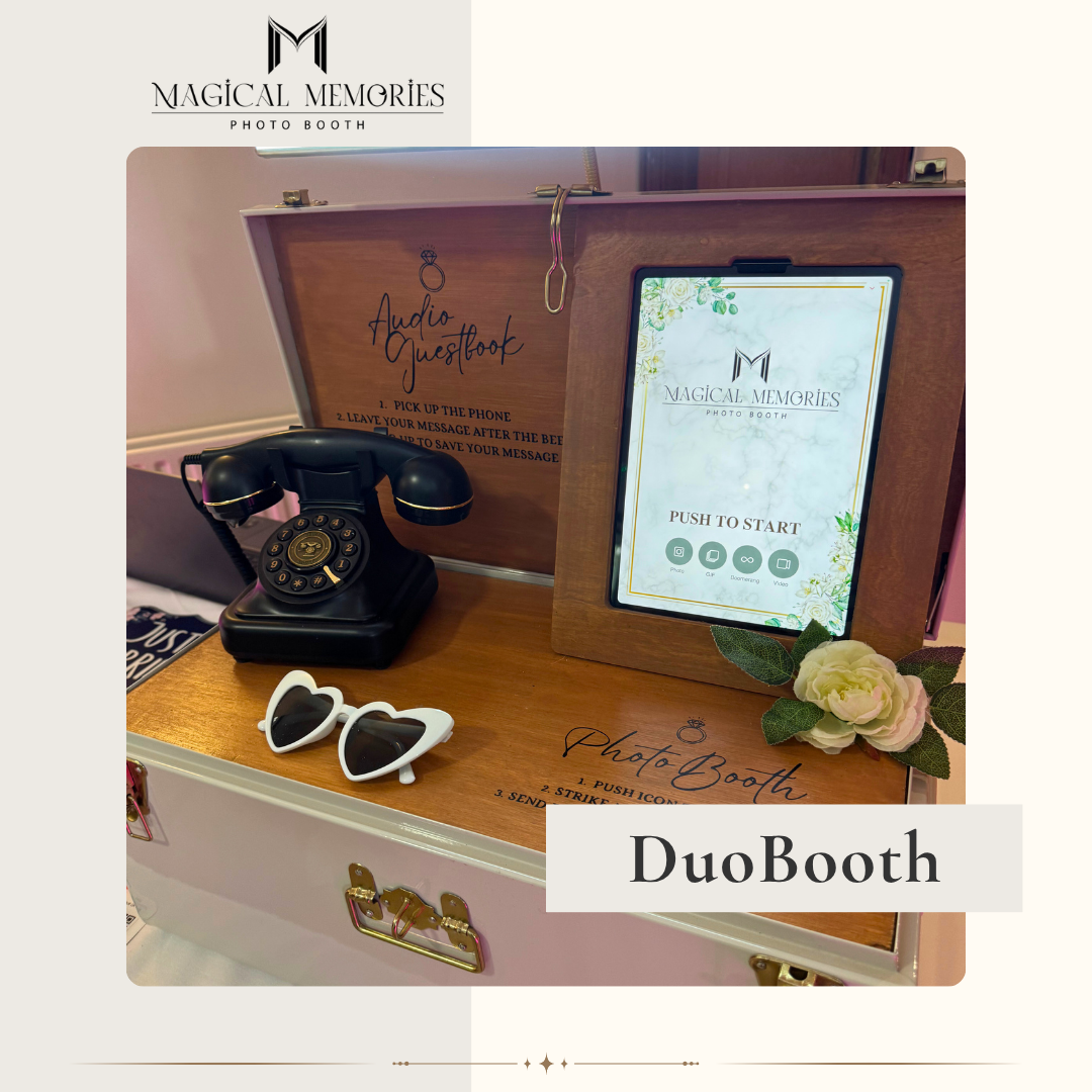 A vintage black rotary phone, yellow heart-shaped sunglasses, and a small floral arrangement sit on a white photo booth box. Behind them, a wooden display has a tablet with 'Magical Memories Photo Booth' and instructions, a chalkboard sign reading 'Audio Guestbook,' and a clear acrylic sign with event details.