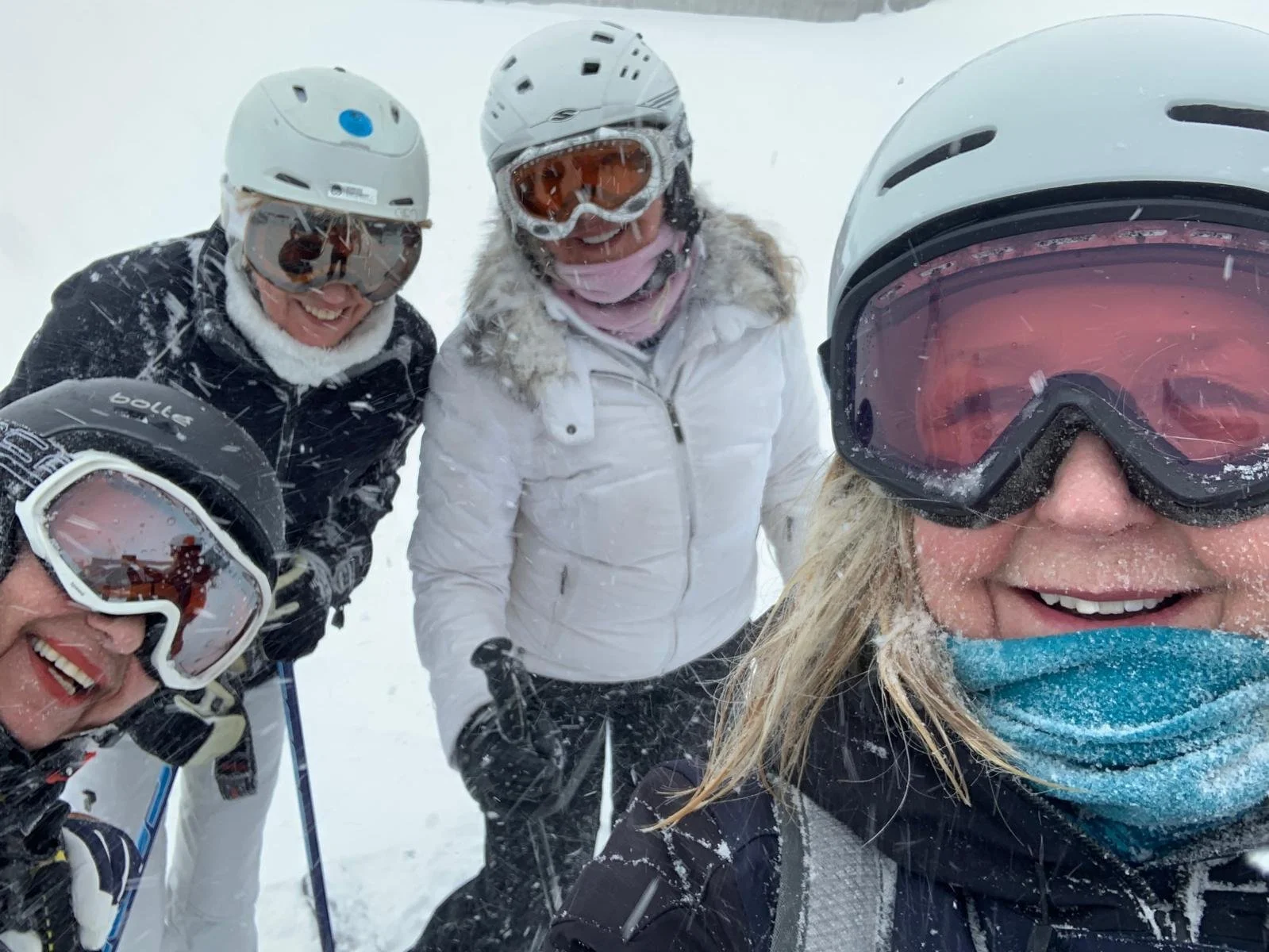 Two women in winter ski gear taking a selfie outdoors in a snowy mountainous landscape during sunset.