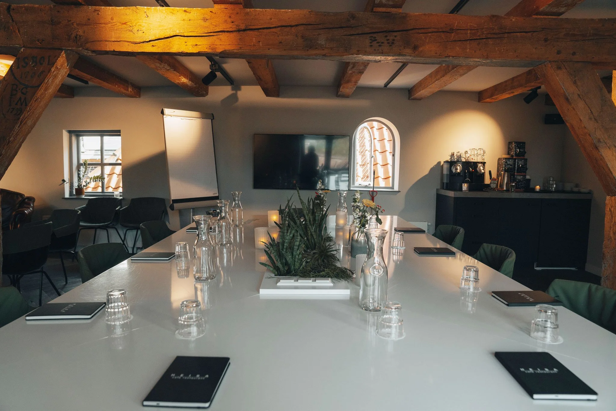 Een grote witte tafel in de vergaderruimte van Heisa, met groene stoelen rondom en robuuste houten balken tegen het plafond.