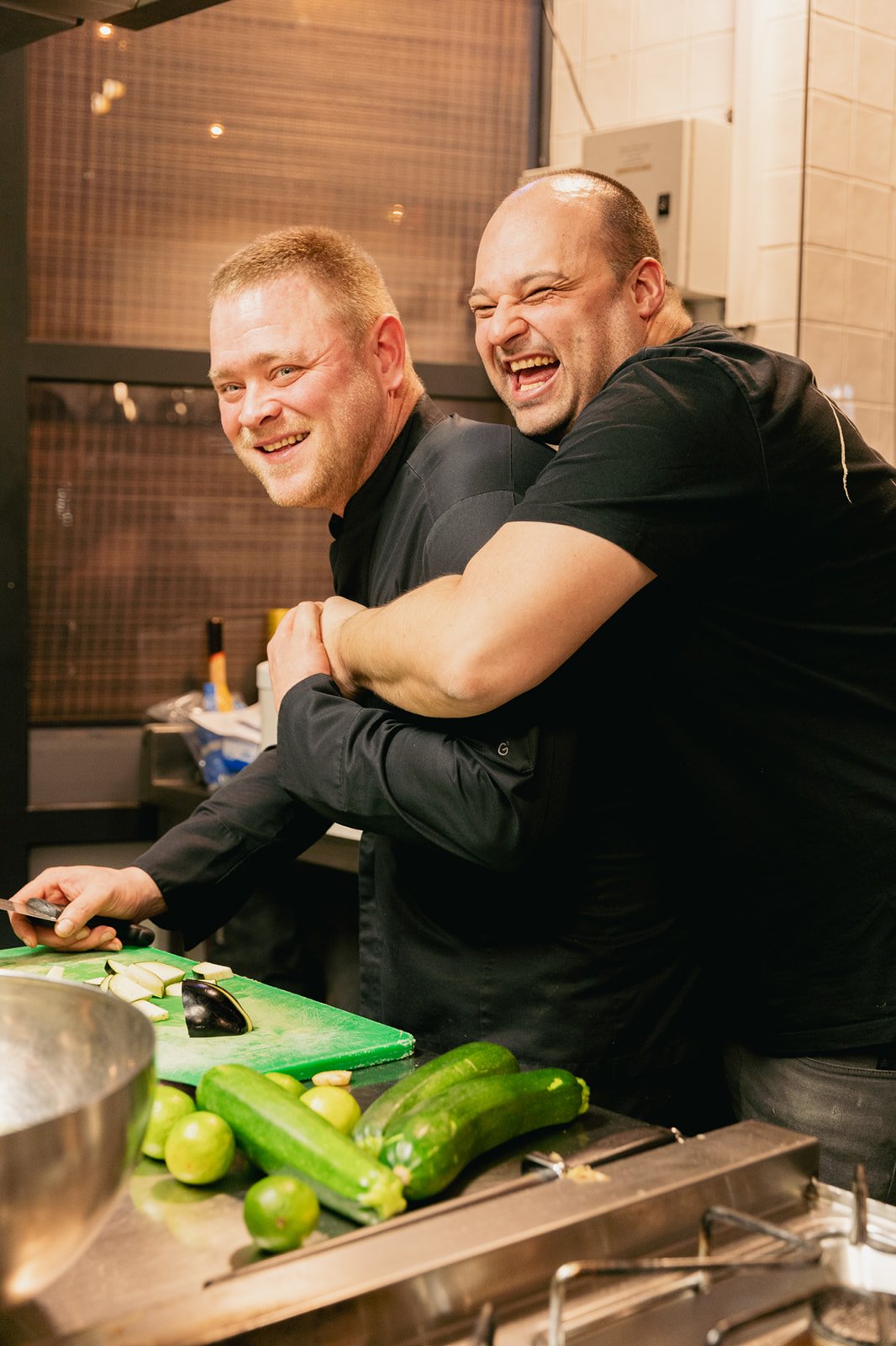 Twee personeelsleden van Heisa in Oudekerk die achter elkaar staan en schaterlachen in de keuken.
