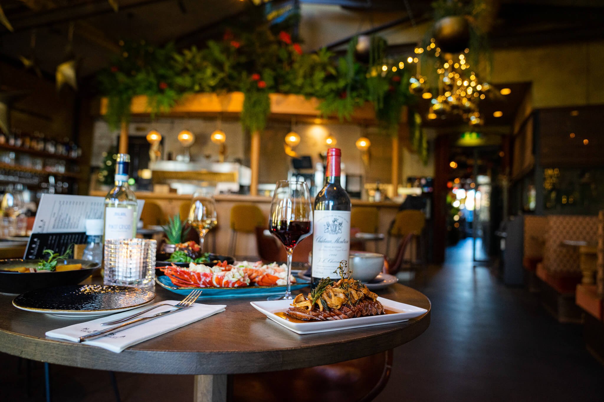 Een gedekte tafel waar lekker eten op staat met op de achtergrond sfeervolle kerstverlichting.