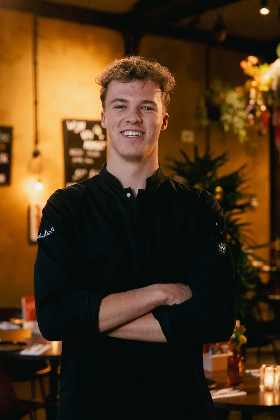 Een personeelslid met blond haar lacht naar de camera en draagt een zwart T-shirt met daarop het logo van Heisa.