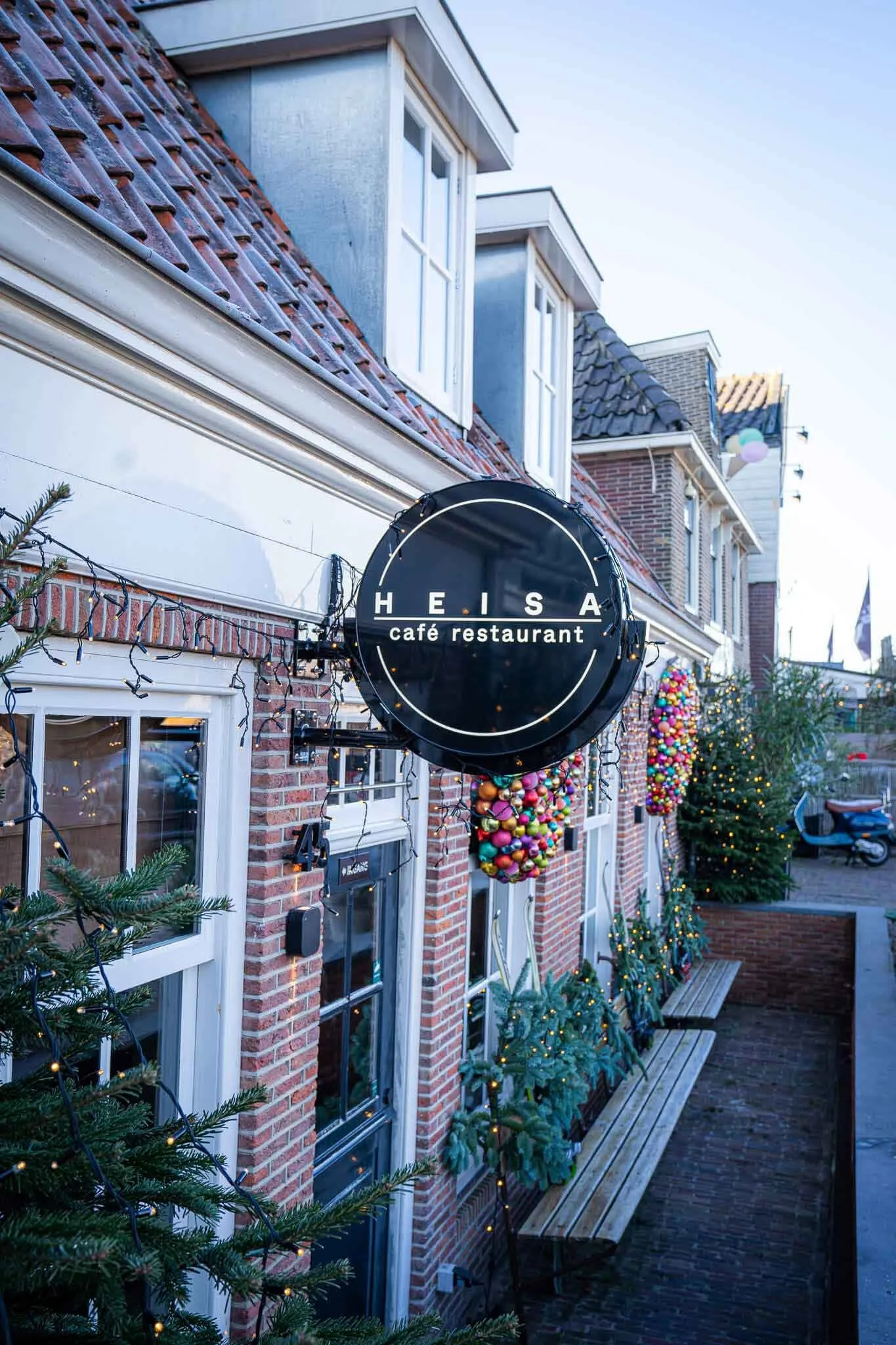 De buitenkant van het restaurant met een zwart rond uithangbord aan de gevel waarop het logo van Heisa staat.
