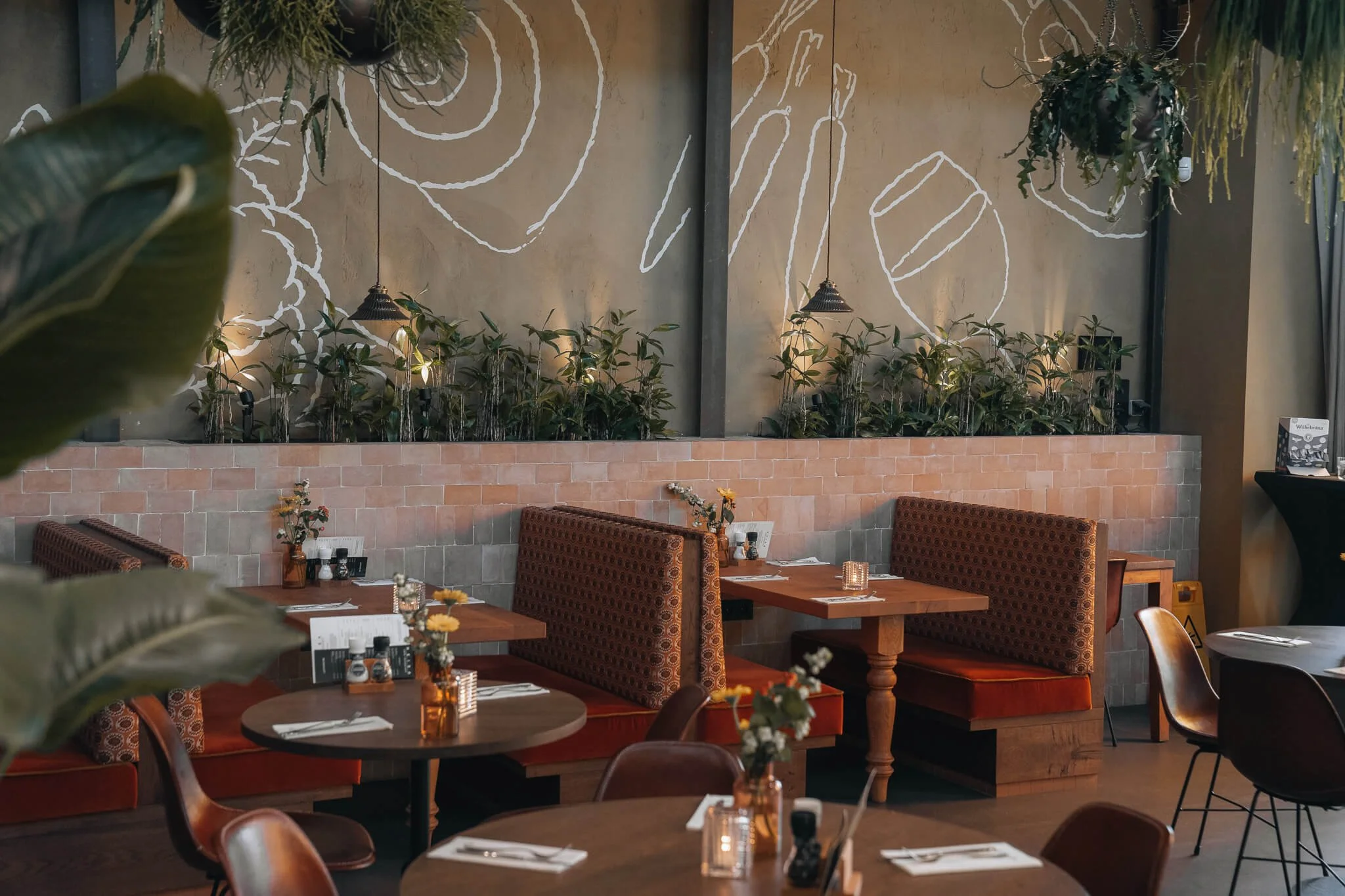 Het interieur van Heisa met een muur vol witte illustraties en houten banken bij tafels die gedekt zijn met servetten en bestek.