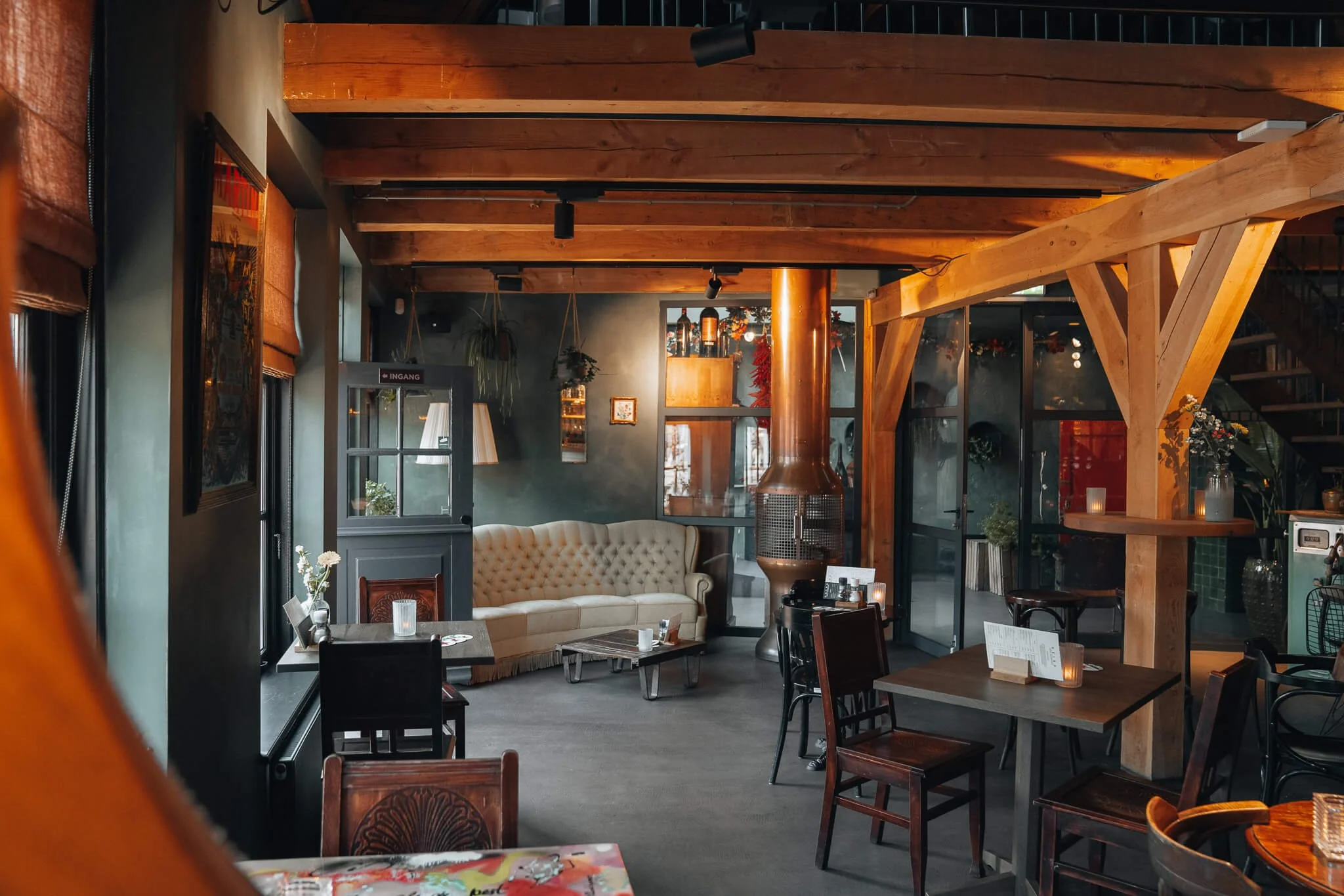 Het interieur van Heisa, met houten balken, een gezellige bank een donkere tafels en stoelen.