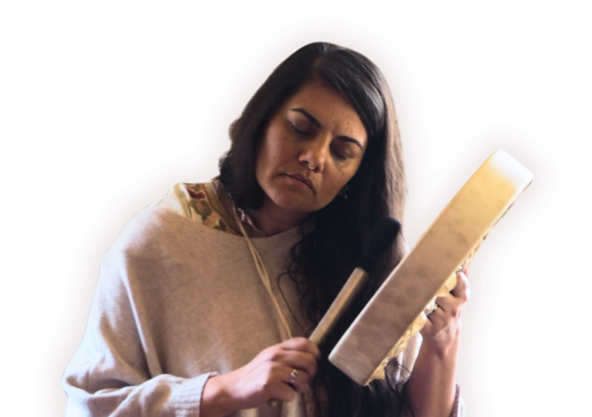 A woman with dark hair wearing a beige sweater with floral accents, looking down at and holding a notebook and a pen.