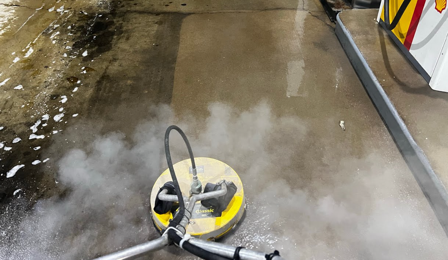 A floor cleaning machine spraying water or cleaning solution on a concrete surface, creating a cloud of steam or mist.