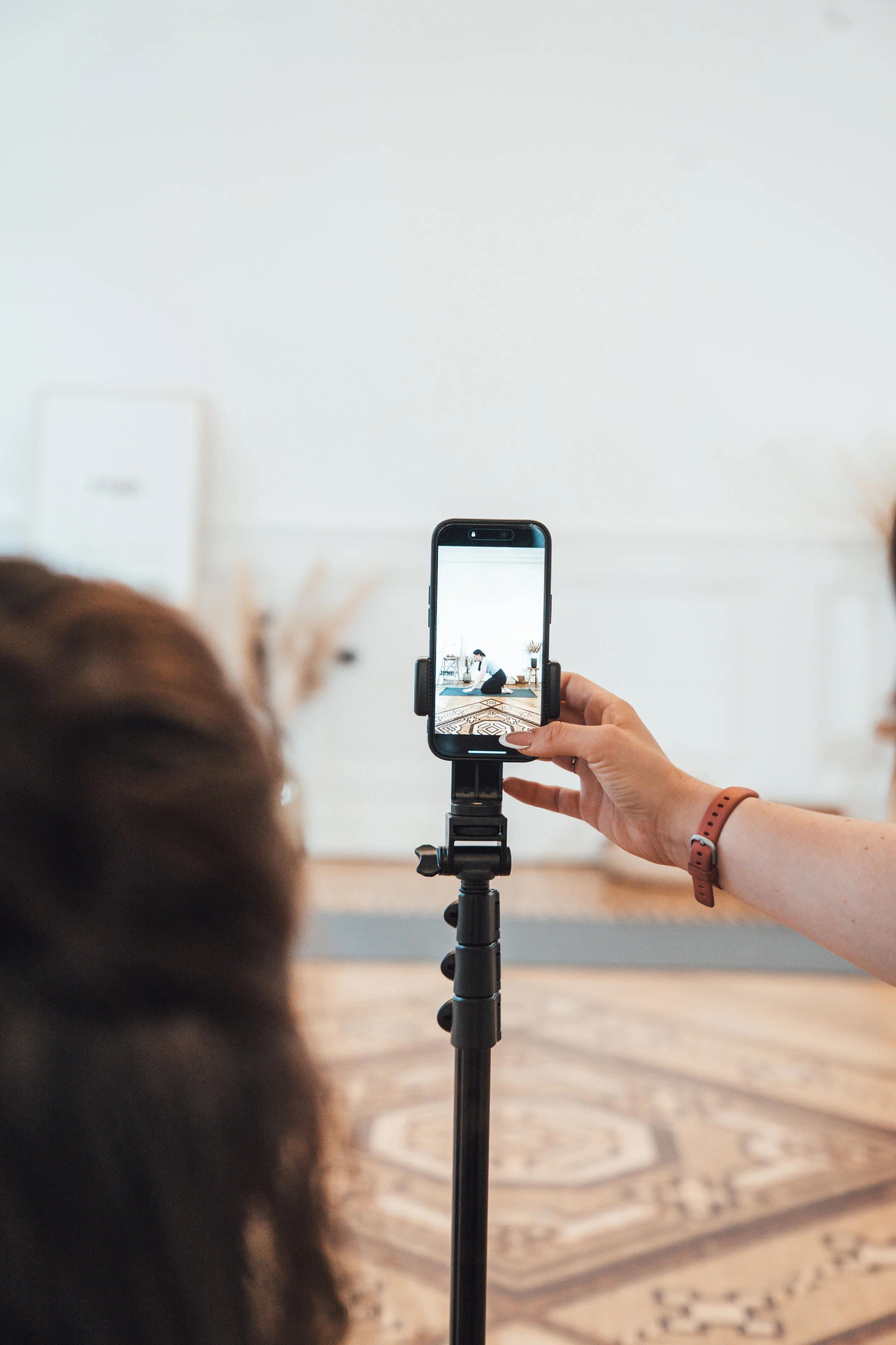 Une personne filme une autre personne en train de faire du yoga dans un intérieur lumineux, avec un smartphone fixé sur un trépied.