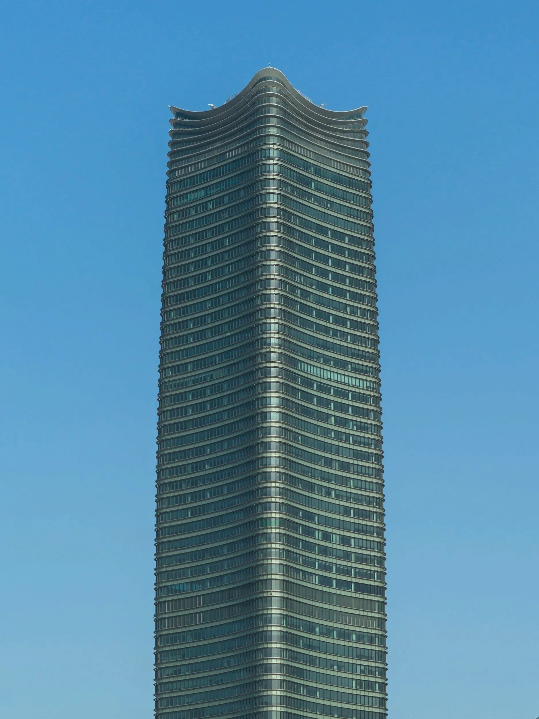 Tall modern skyscraper with curved, wavy top against a clear blue sky.
