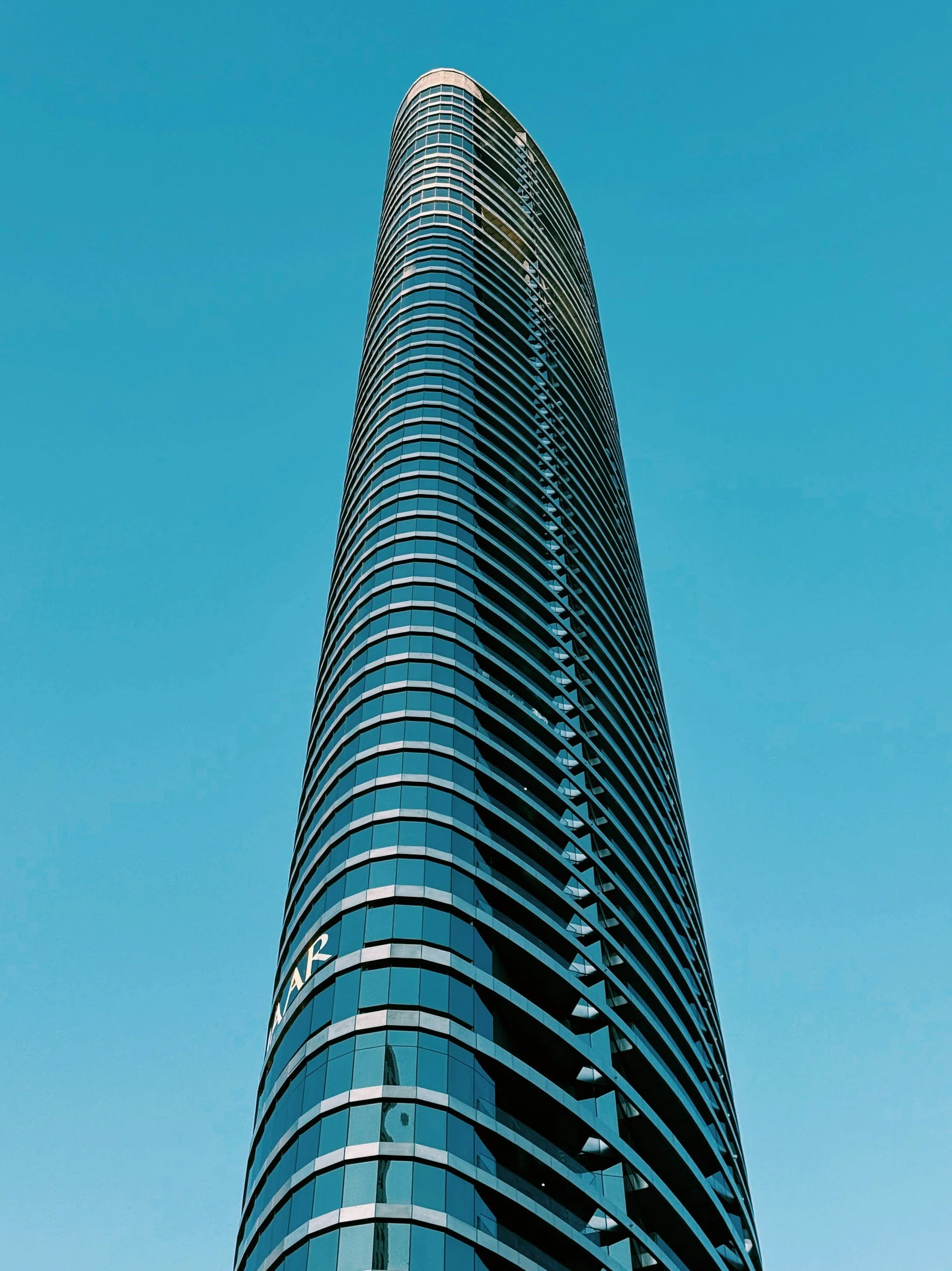 A tall modern skyscraper with a curved glass facade against a clear blue sky.
