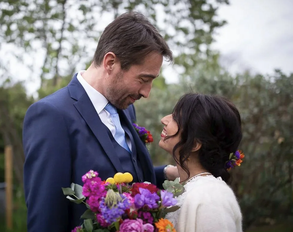 Un couple lors d'un mariage, la femme tient un bouquet de fleurs colorées, ils se regardent en souriant pendant un reportage photo de mariage à Paris.