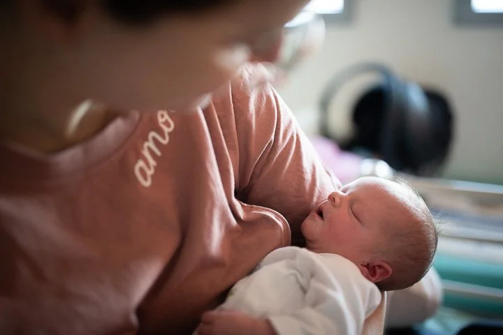 Une personne tient un nouveau-né contre elle dans une pièce domestique. Photo prise par Marie Pierson pendant un reportage de photos d'accouchement à Paris.