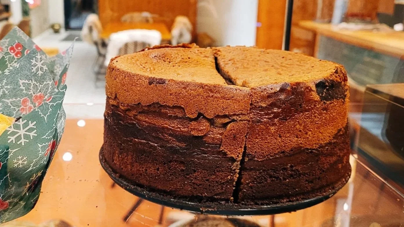 Een grote chocolade- en vanille cake op een tafel in een bakkerij of café, met een snee eruit.