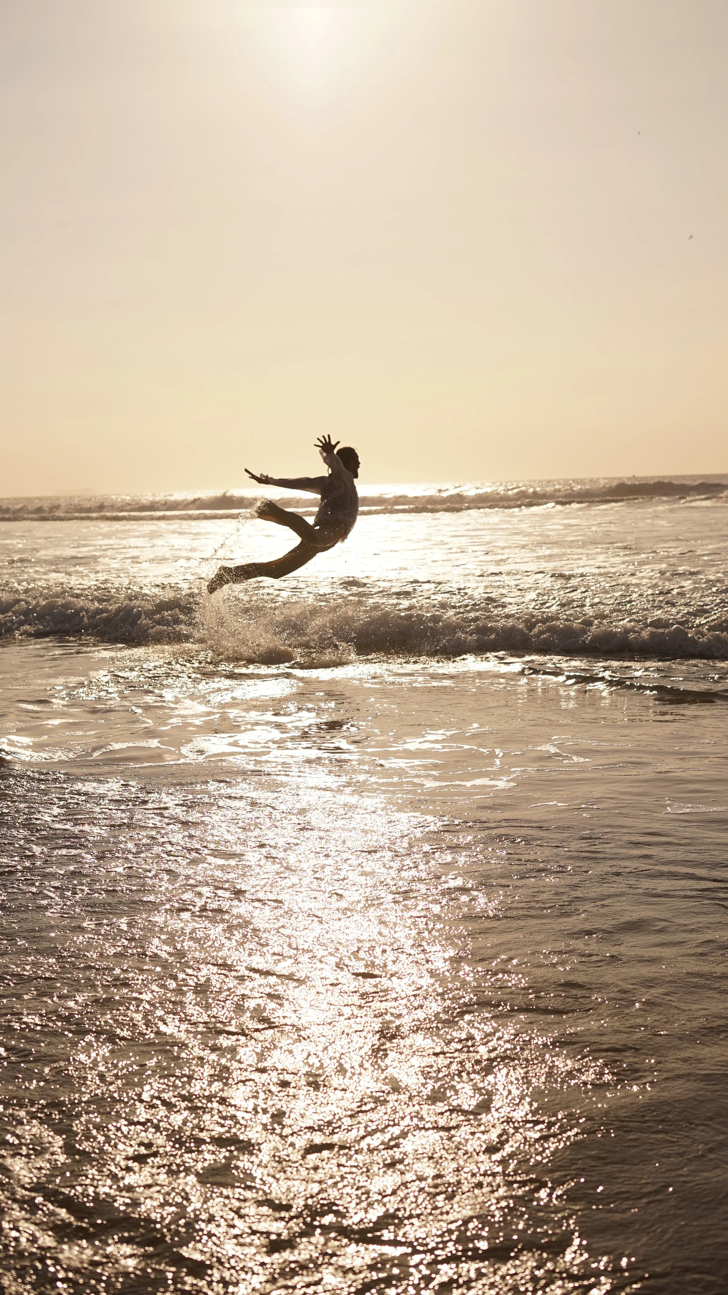 Pessoa pulando na água do mar ao pôr do sol.