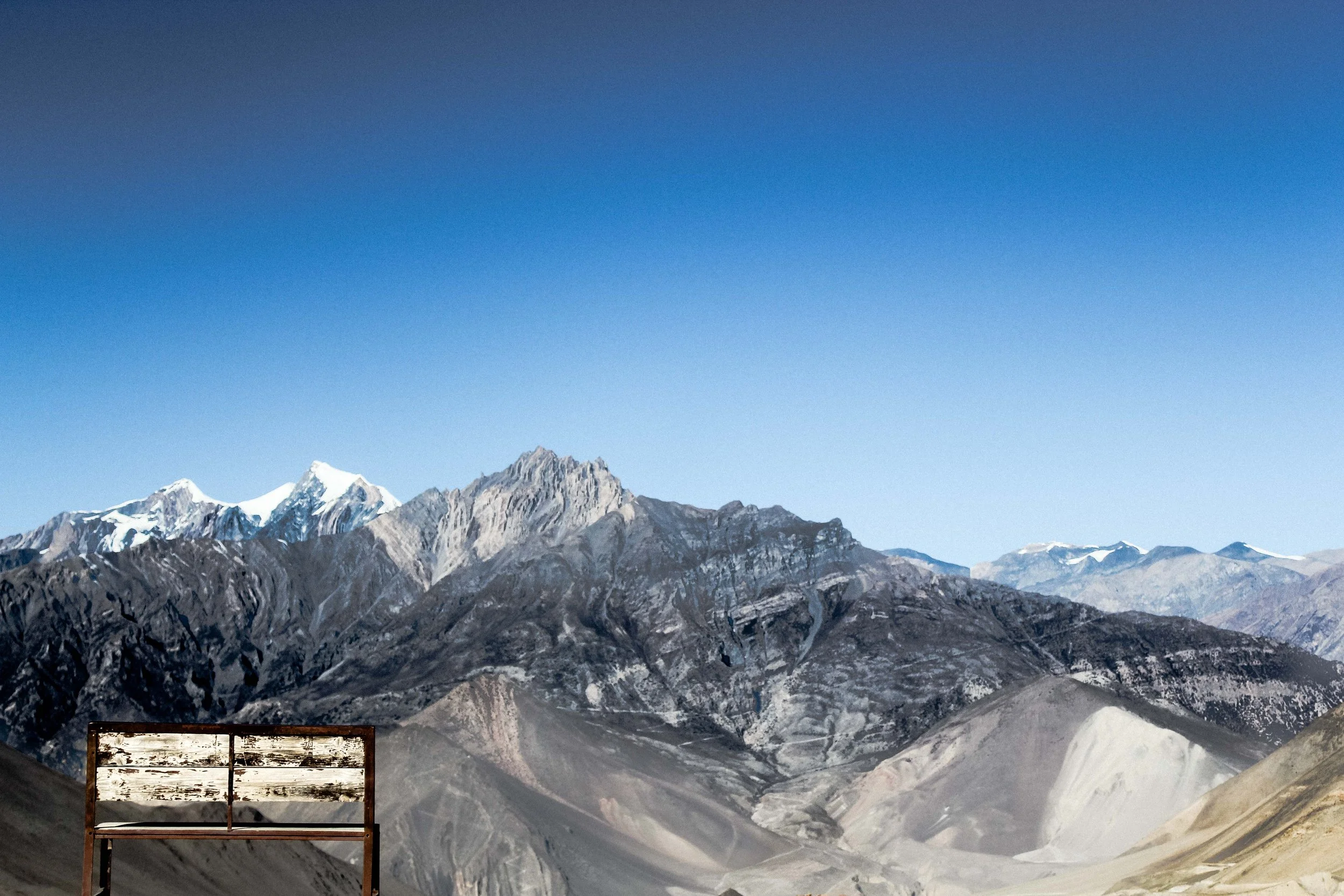 Montanhas nevadas sob céu azul com uma cerca de madeira ao primeiro plano.