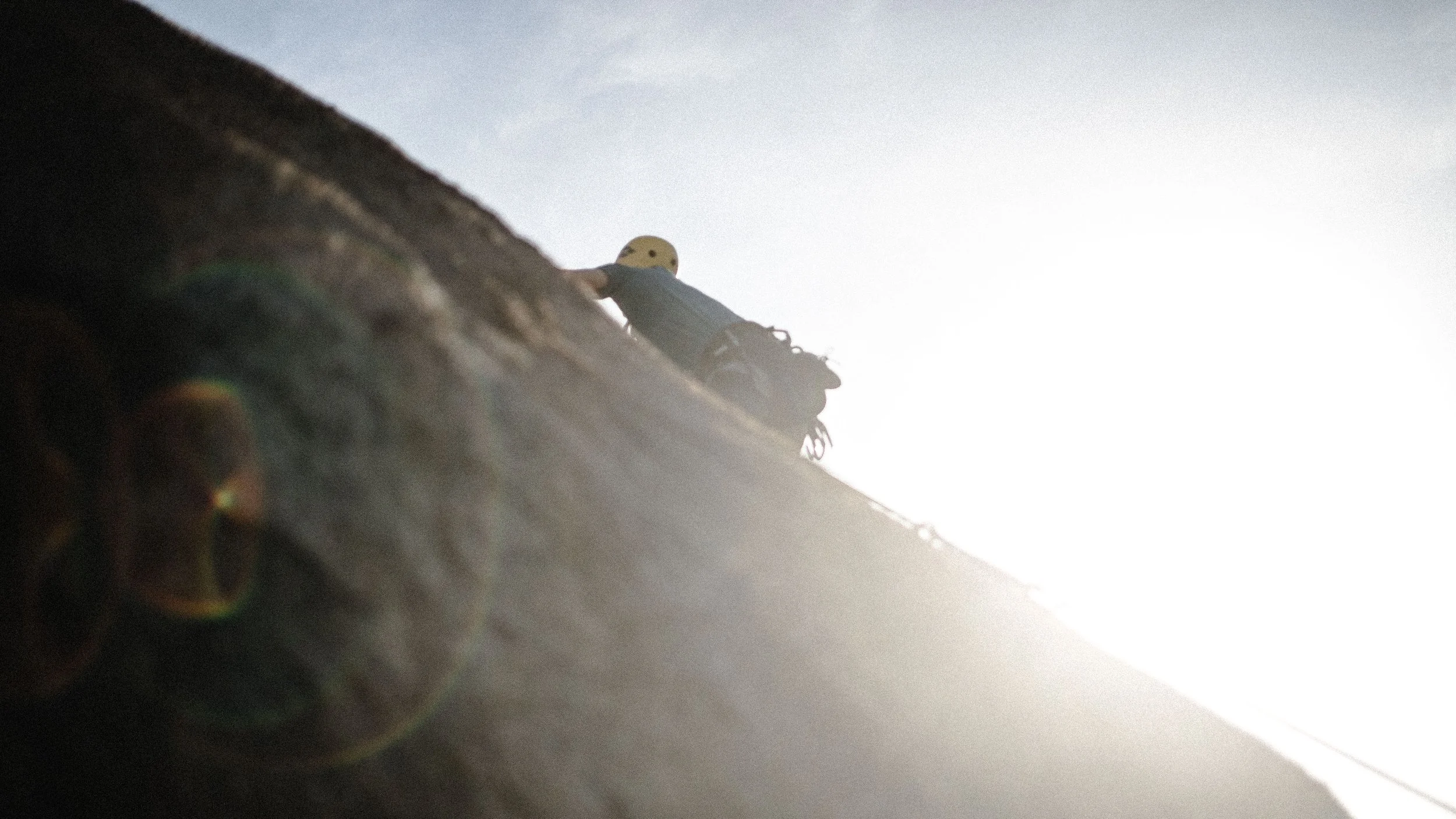 Pessoa escalando uma parede de rocha sob luz solar forte, usando capacete e equipamento de escalada.