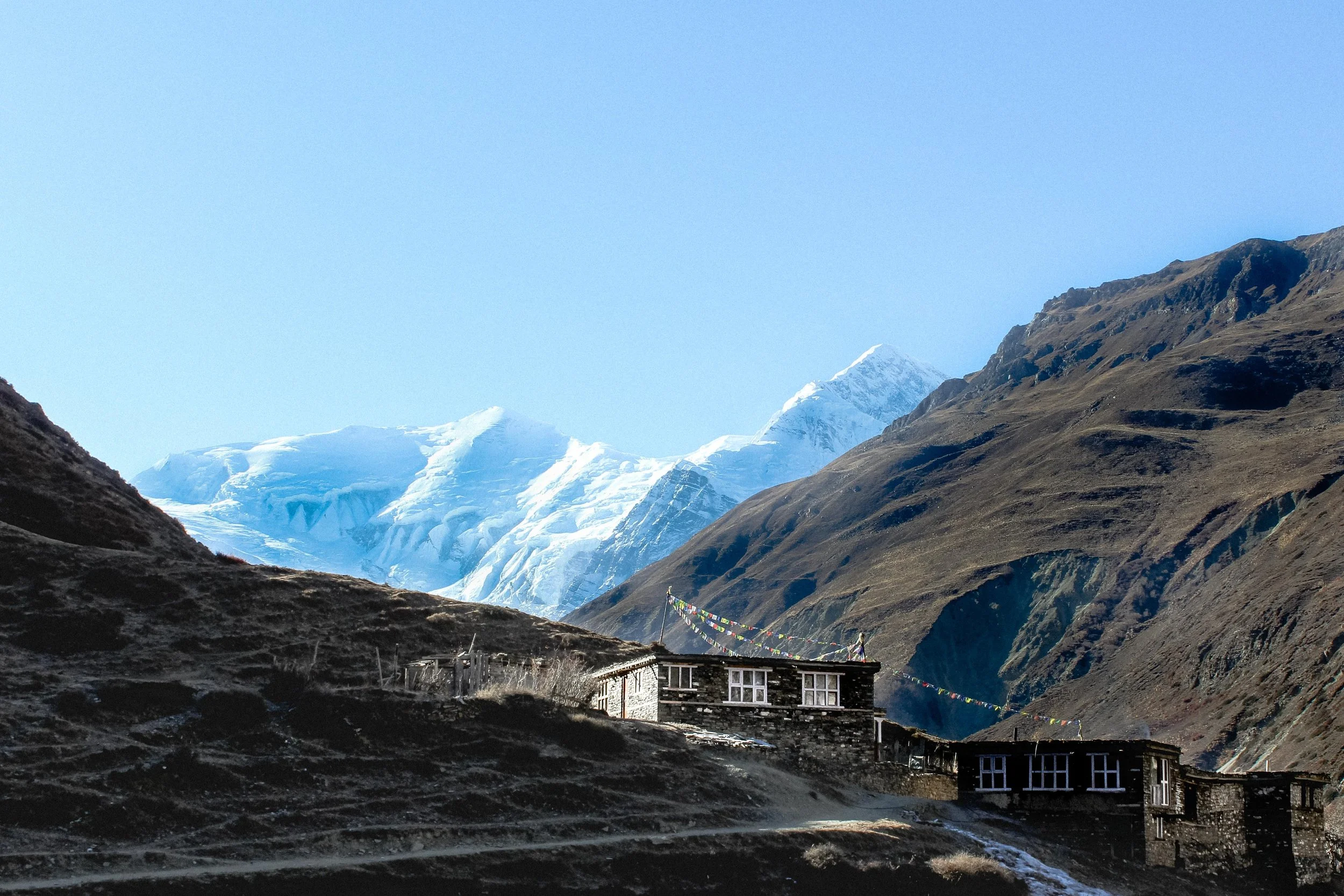 Casas de pedra em uma região montanhosa, ao fundo há picos de montanhas com neve e gelo.