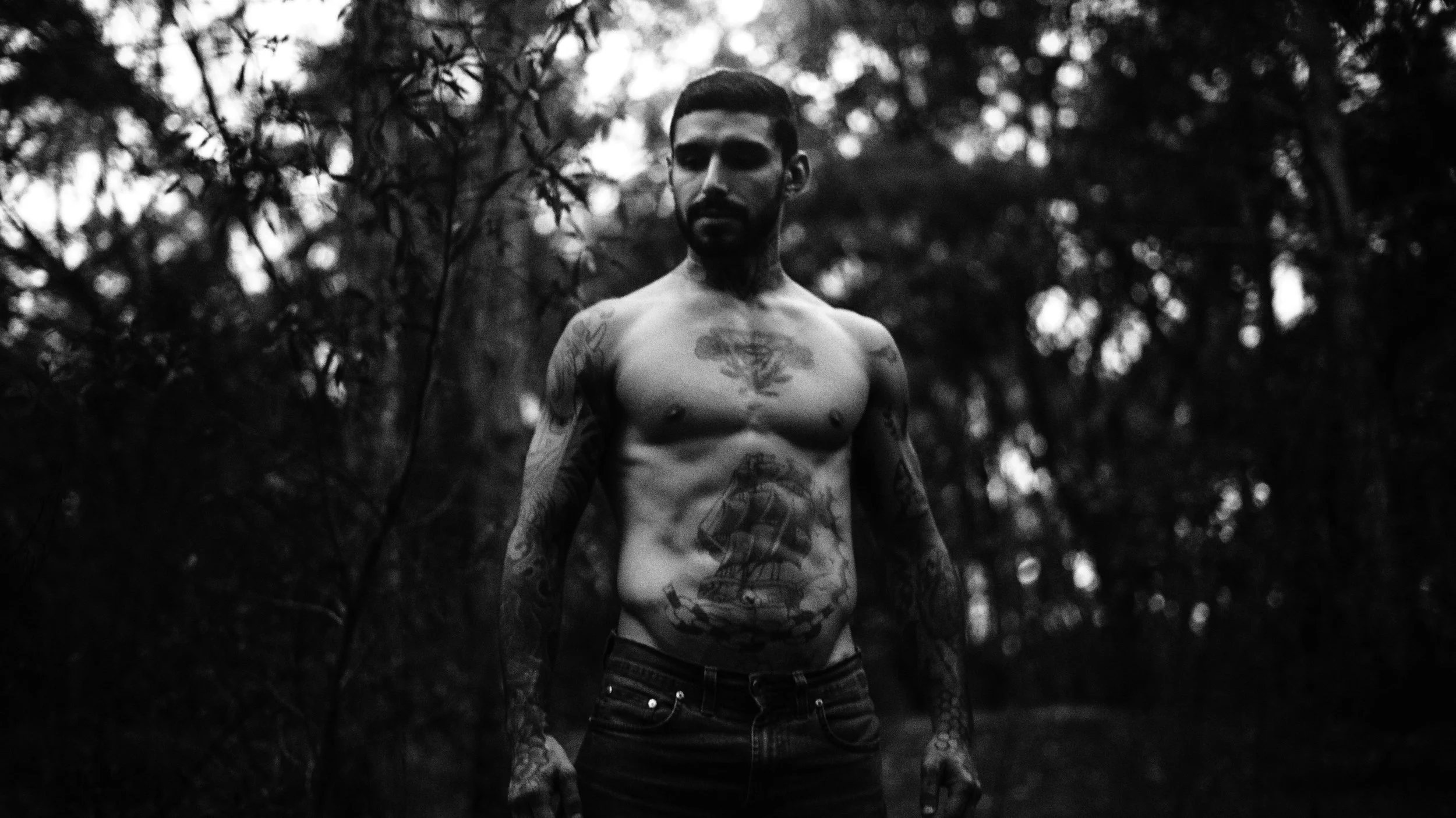 homem com tatuagens no corpo, sem camisa, em uma floresta, em preto e branco