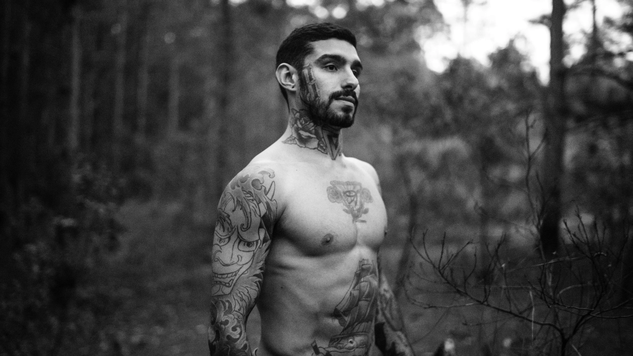 Homem tatuado sem camisa em um cenário natural de floresta
