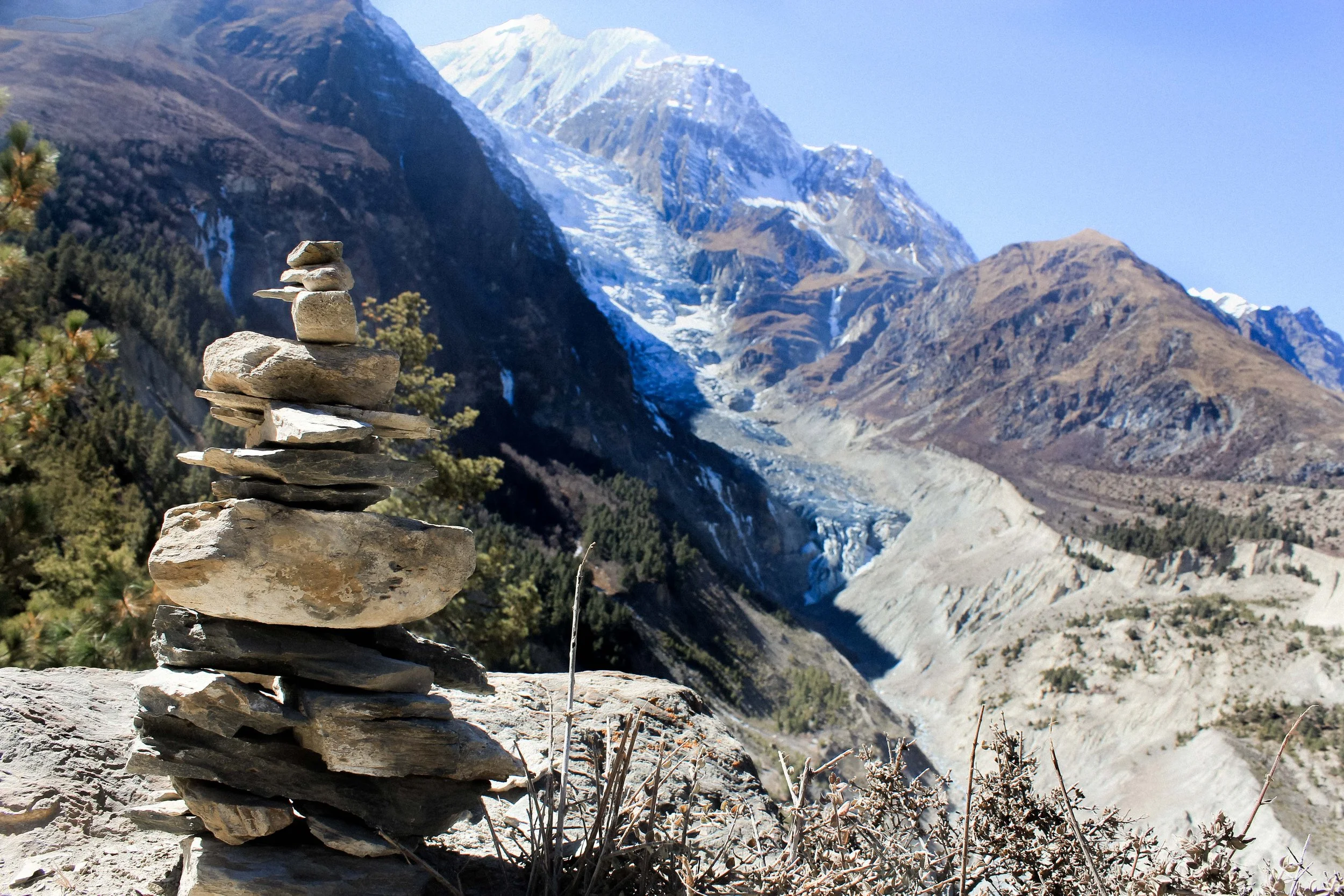 Estação de pedra empilhada na montanha com glaciares e picos nevados ao fundo.