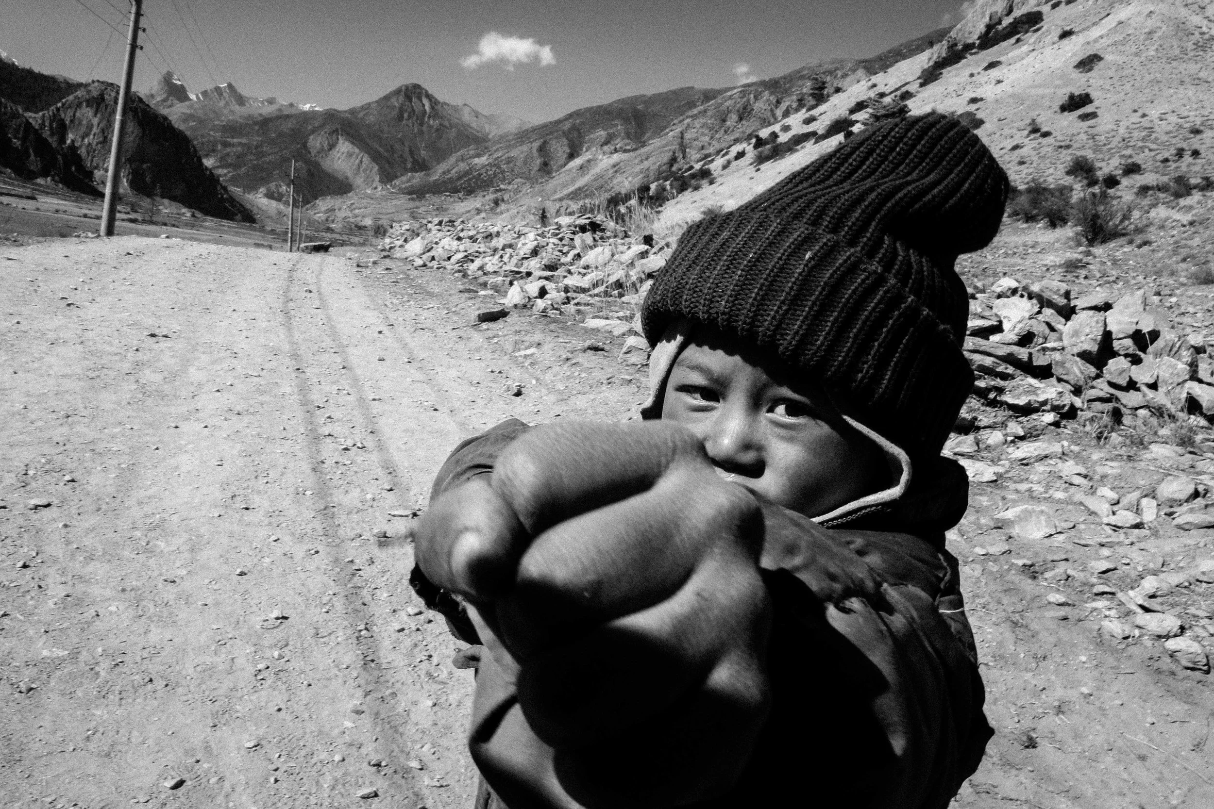 Criança com gorro de lã apontando para a câmera em um ambiente montanhoso ao ar livre.
