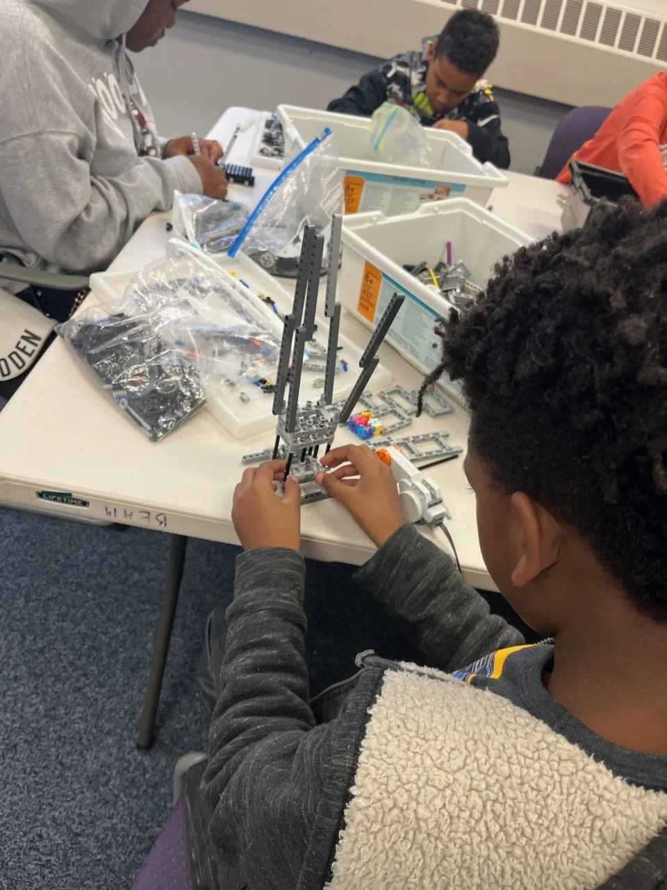 Children assembling LEGO sets at a table in a classroom