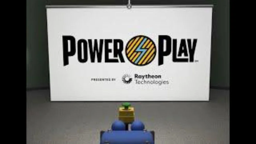 A Lego robot facing a Power Up sign with logos of Raytheon Technologies and Power Play on it in an indoor setting.