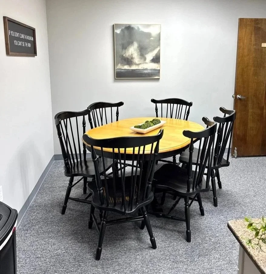 A kitchen with a round table and four black chairs, a white countertop with appliances, a coffee station, and a sliding glass door leading outside.